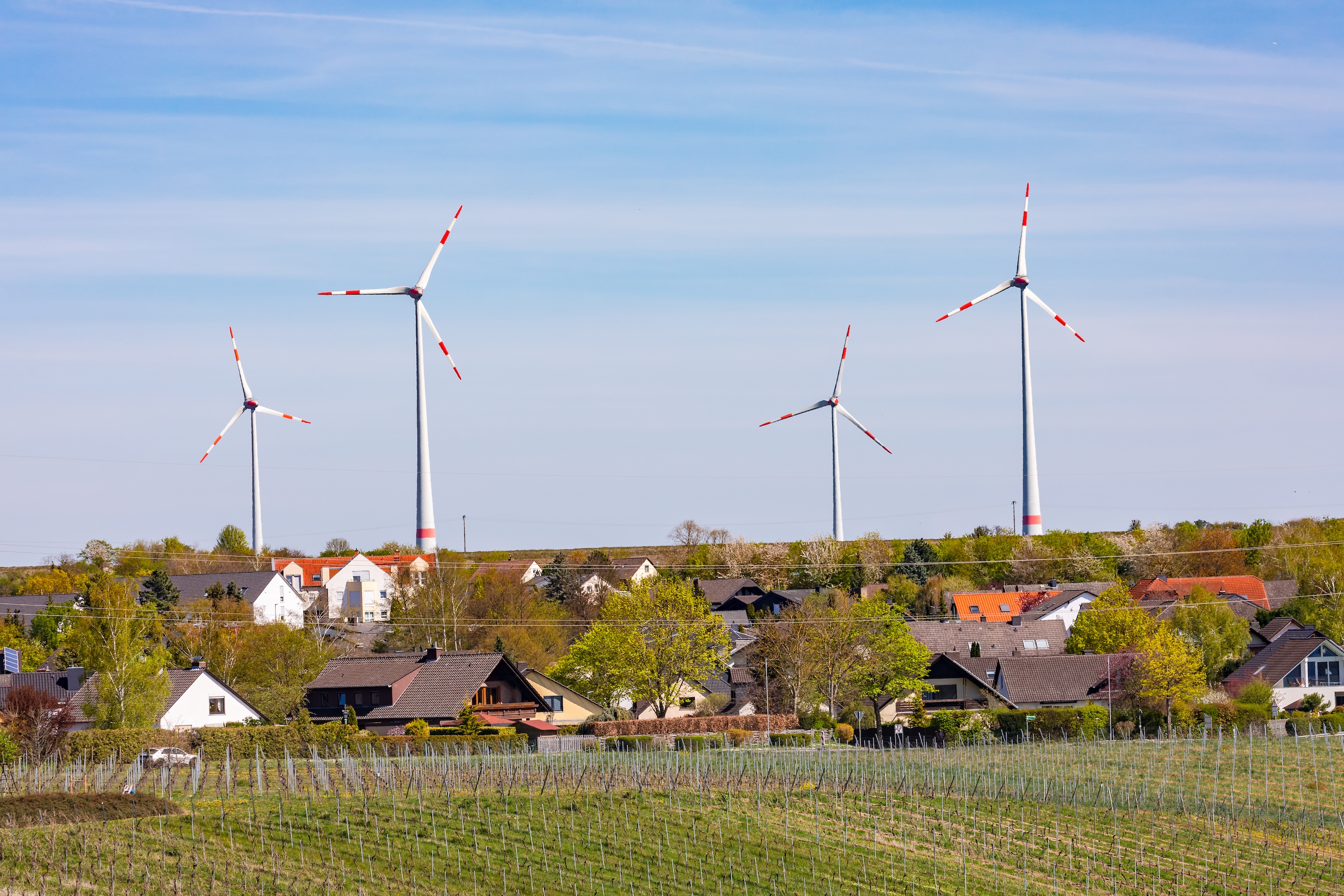 Four wind turbines against a blue sky stand over a rural town with red-topped buildings