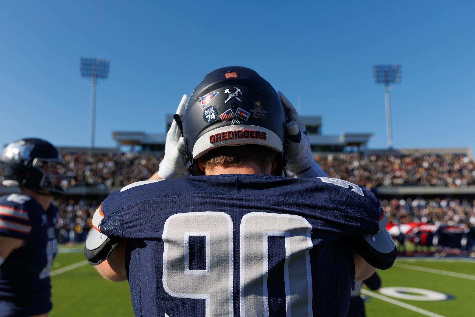 Colorado School of Mines football player in uniform adjusting helmet