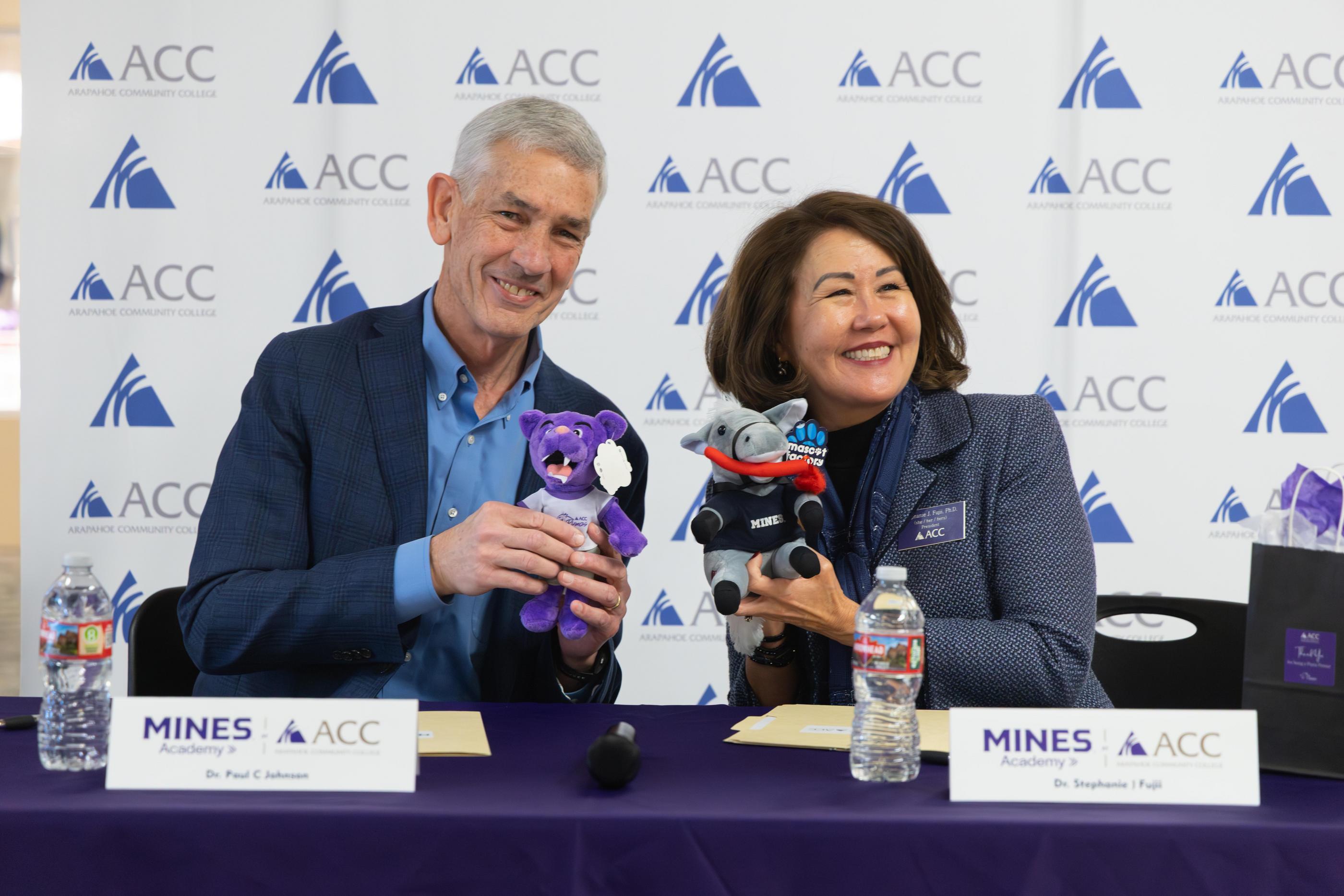 Mines President Paul C. Johnson and ACC President Stephanie J. Fujii sit at table holding mascot plushies