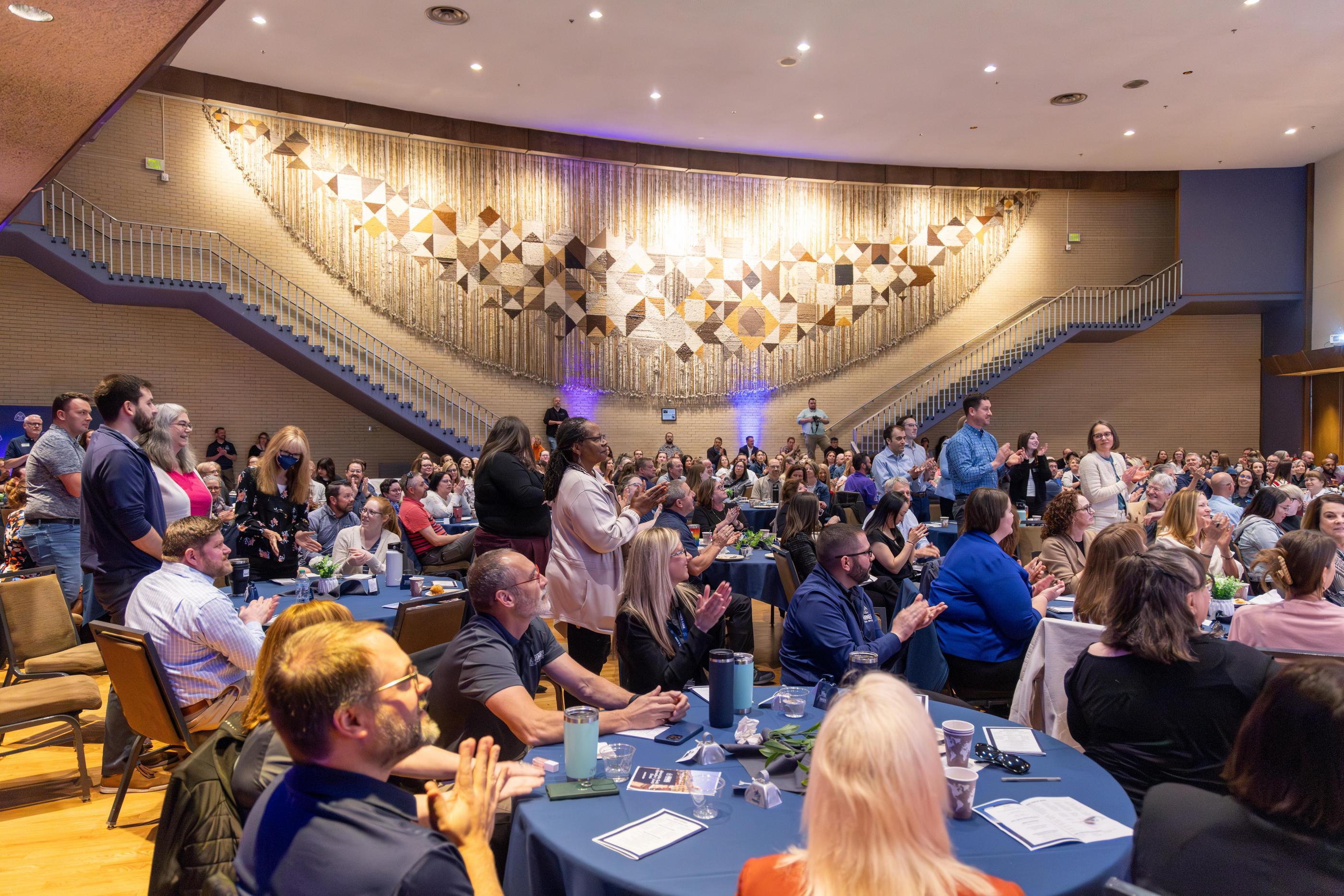 groups of people sitting at tables and clapping in Friedhoff Hall