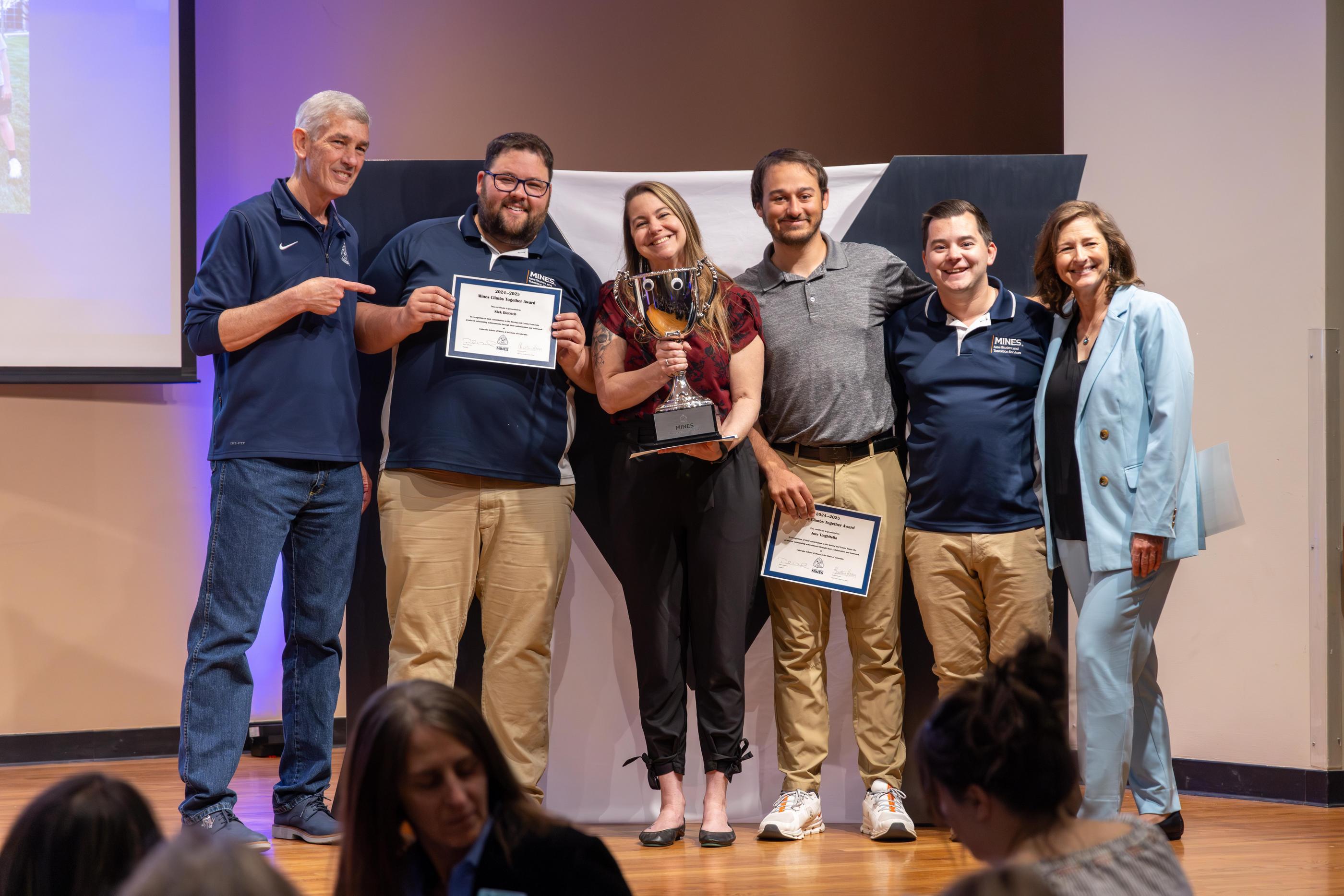 Group photo of Mines employees with President Johnson holding up an award