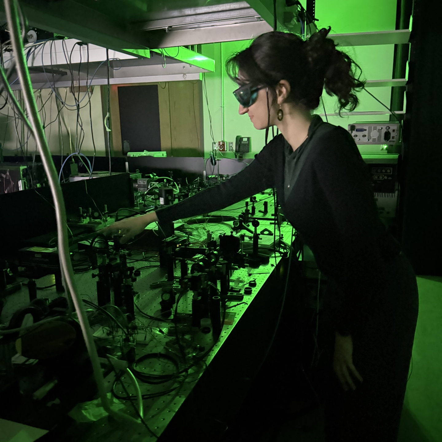 Female student works in a quantum laboratory lit by green light