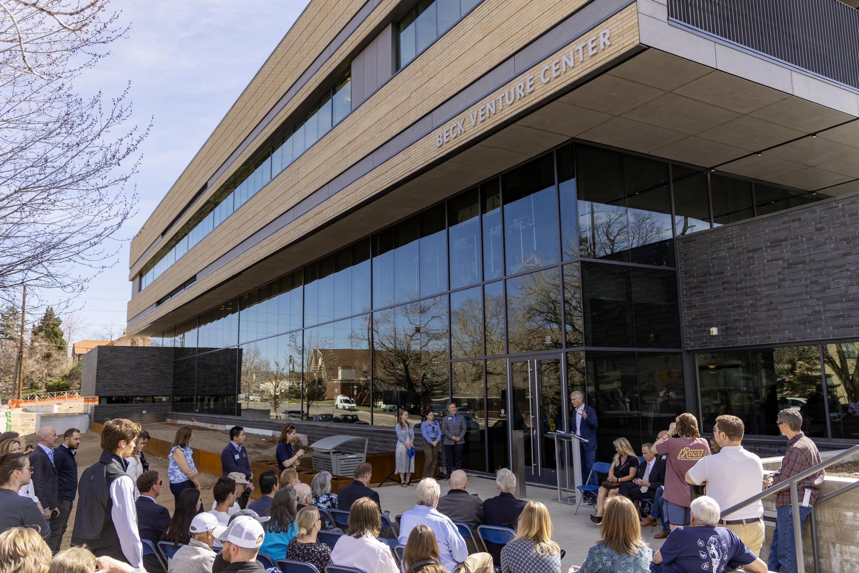 A crowd of people stand outside the main entrance to the Beck Venture Center