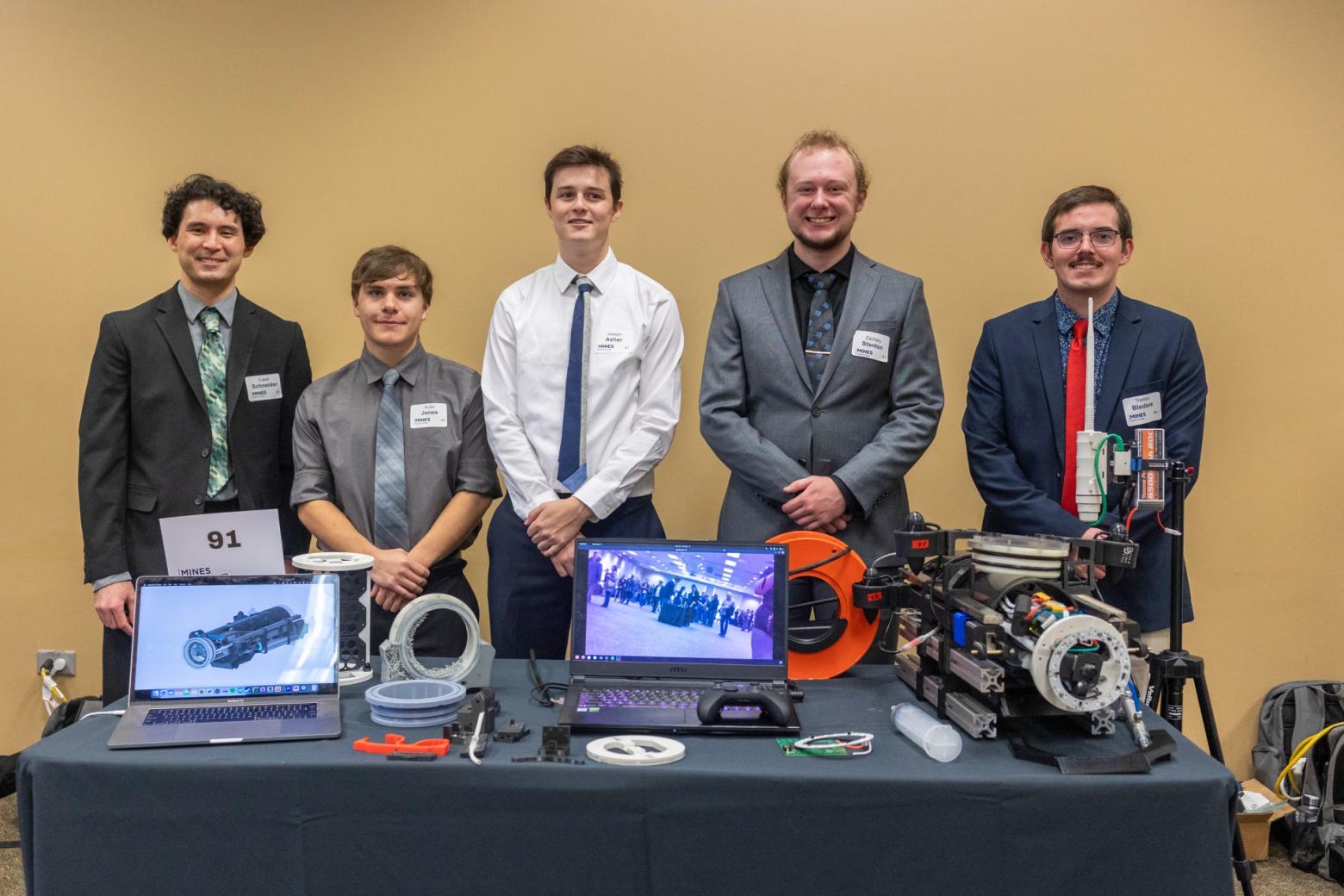 Five Mines students stand in front of a table with elements of their capstone design project that collects ocean subsurface data.
