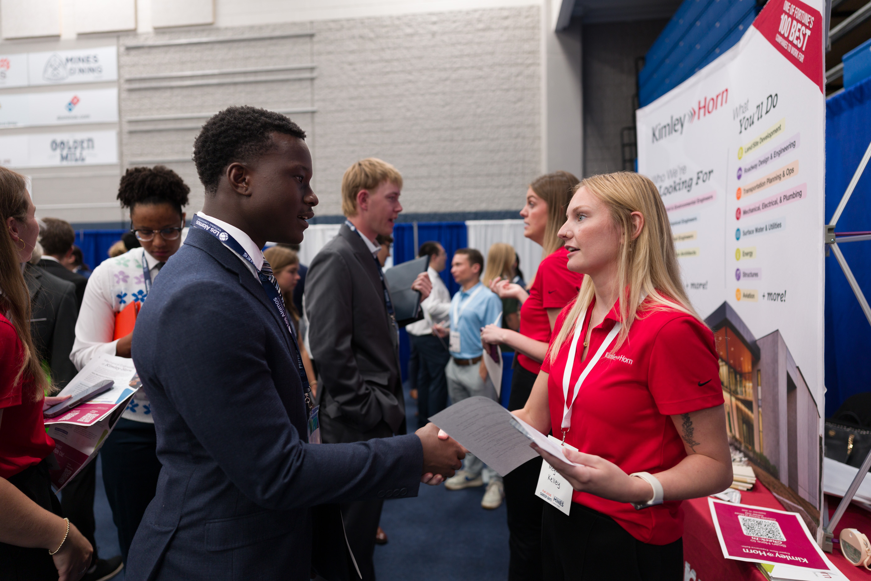A student in a navy suit shakes hands with a Kimley-Horn recruiter in a red polo who holds his resume