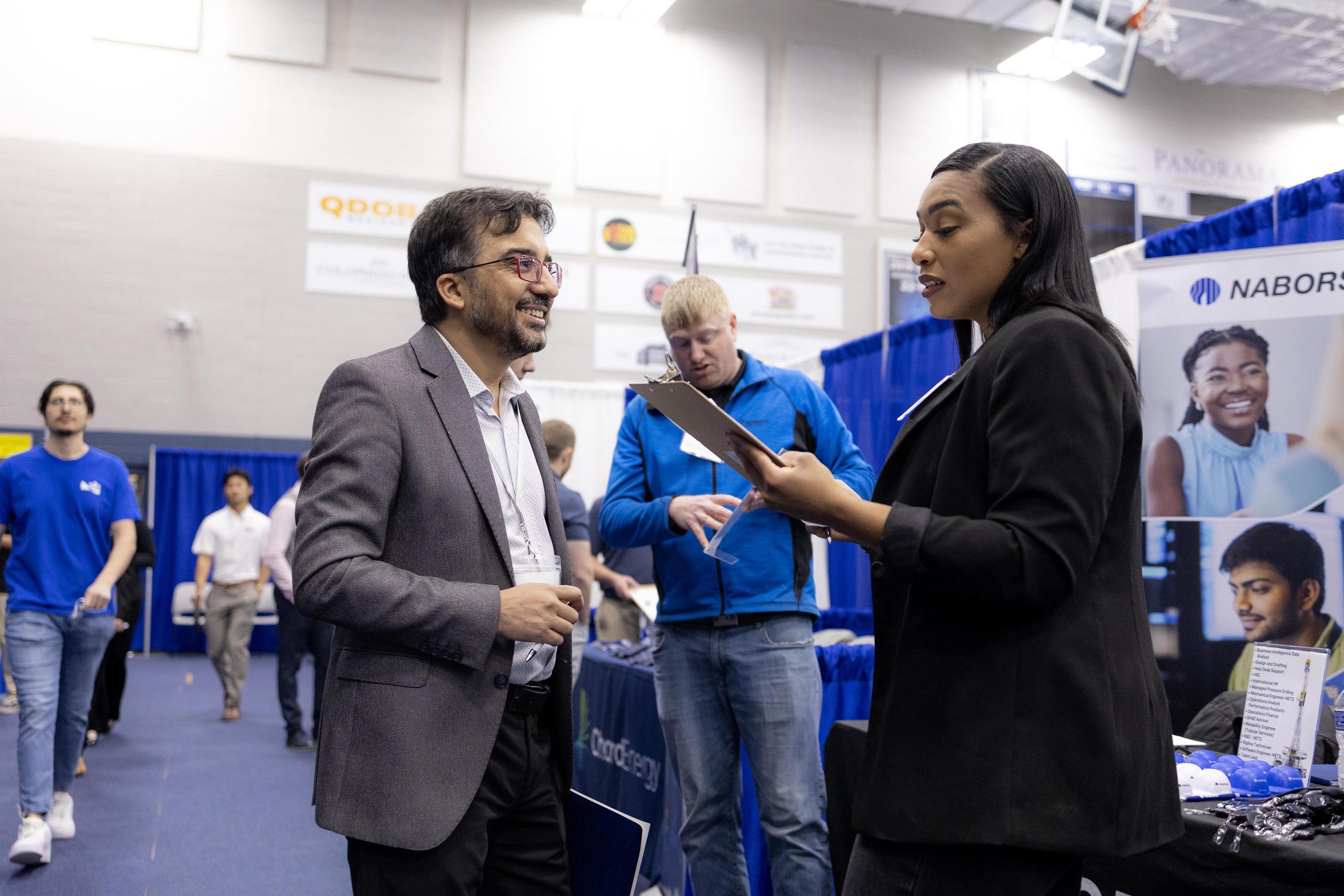 A recruiter holding a clipboard talks with a student