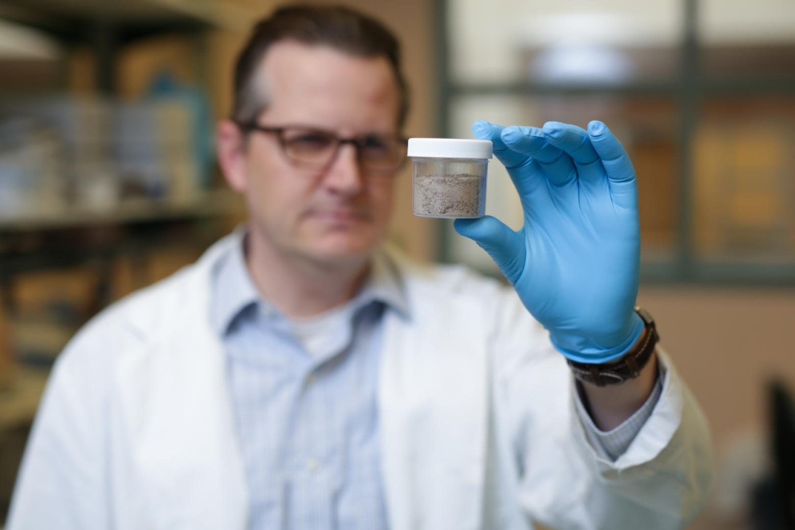Chris Higgins, University Distinguished Professor of Civil and Environmental Engineering at Mines wears a white lab coat and holds a PFAS sample.