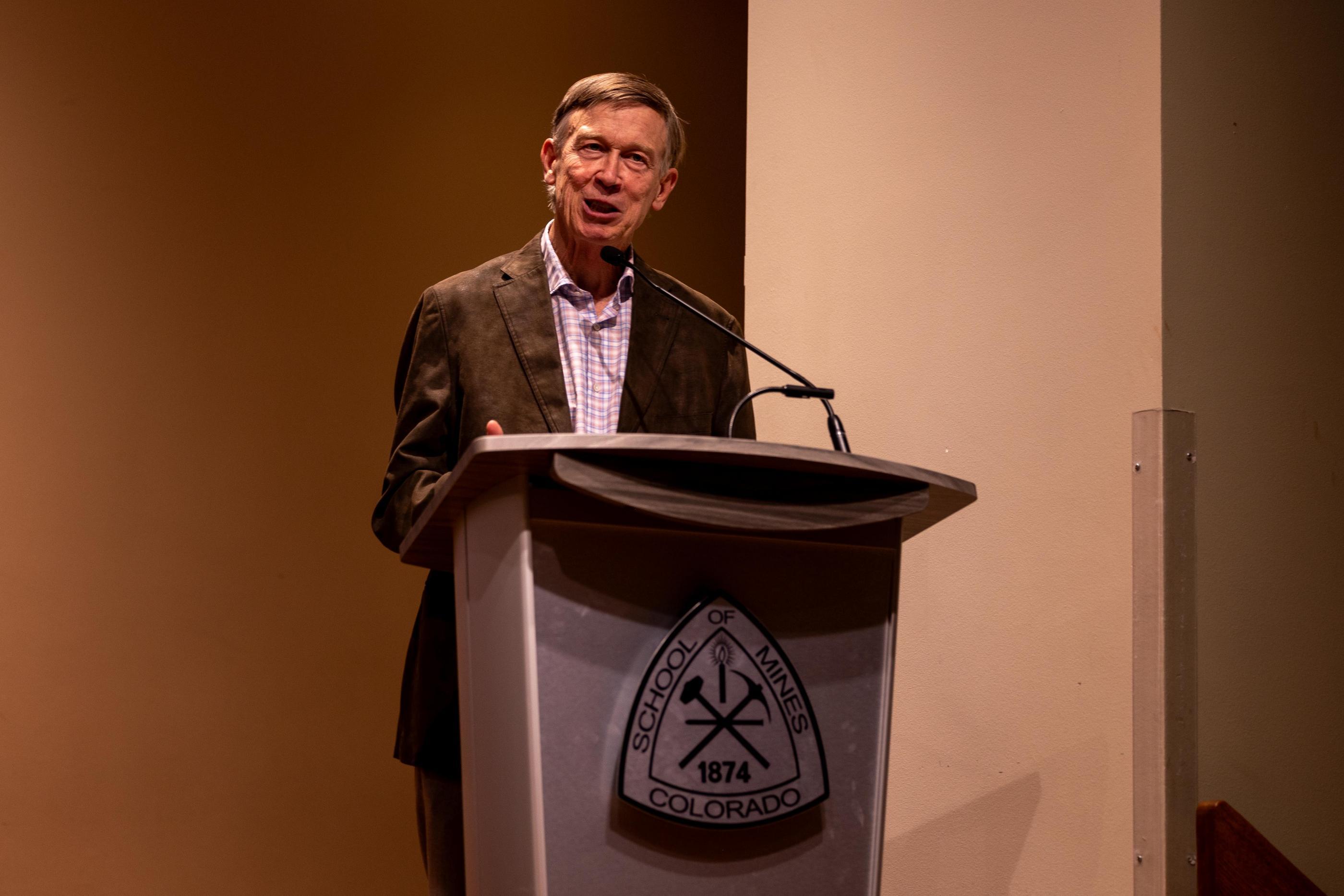 John Hickenlooper stands at a podium at Critical Minerals Symposium