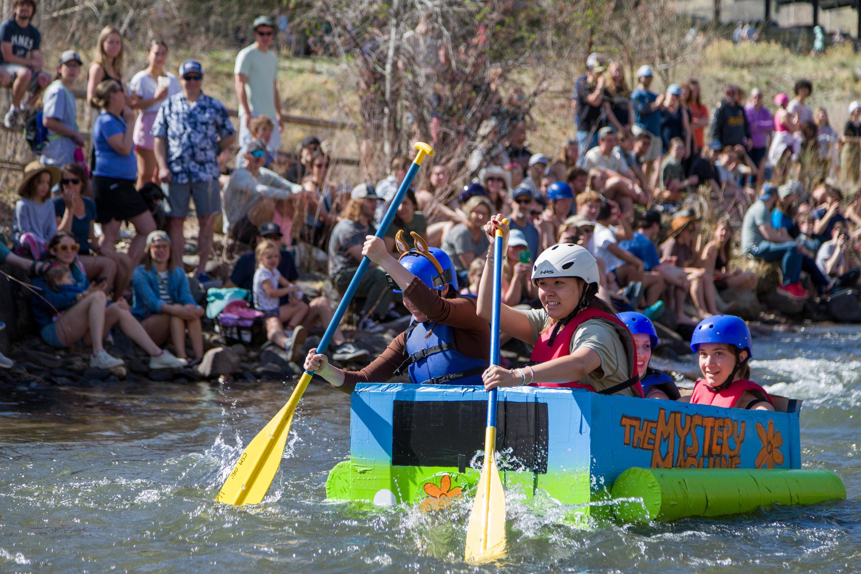 students paddle a cardboard boat that looks like the Mystery Machine