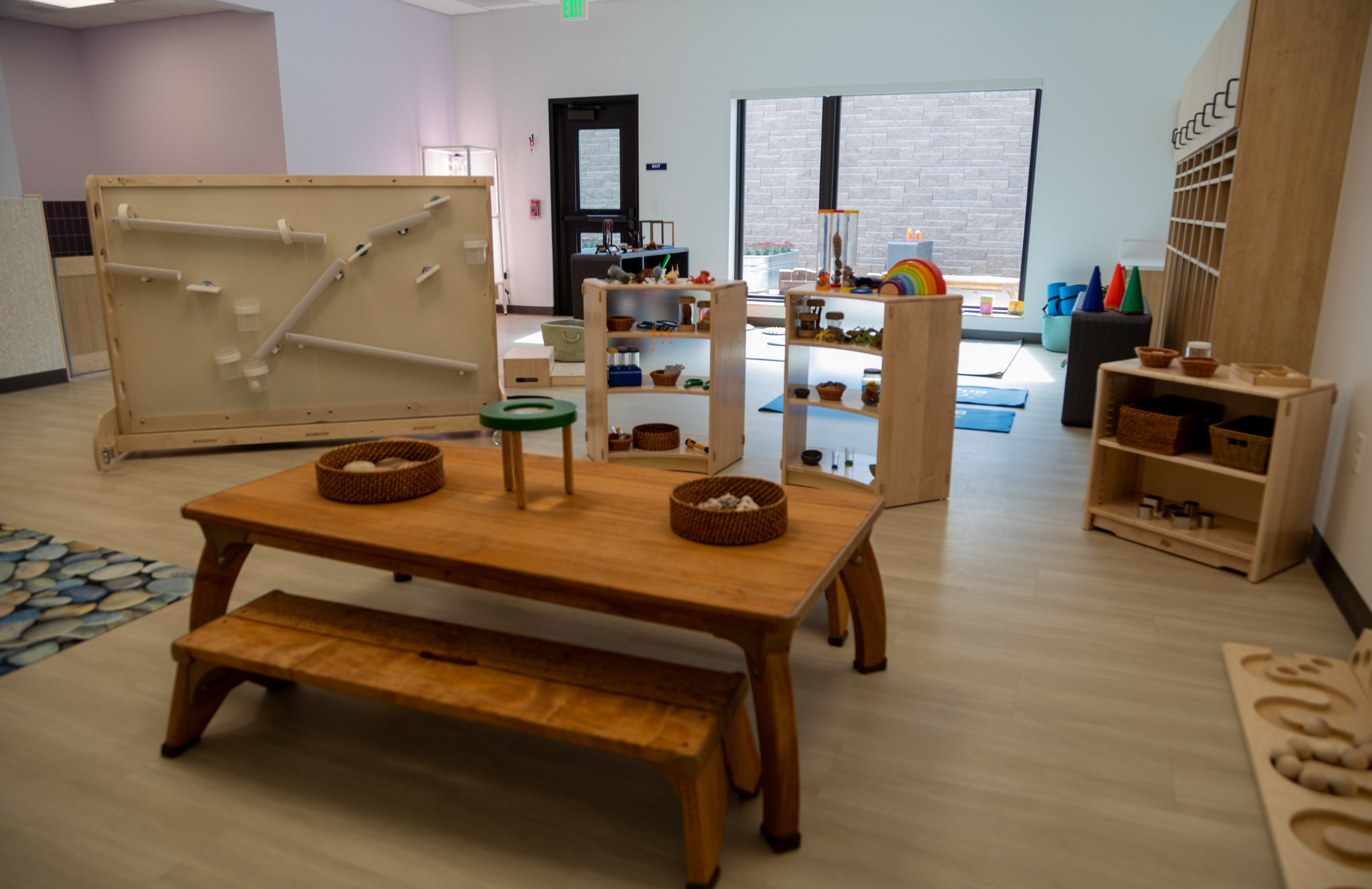 A sensory play area at the Mines Early Childhood Center with a wooden ball-track panel, low shelving stocked with natural materials and a child-sized table and bench.