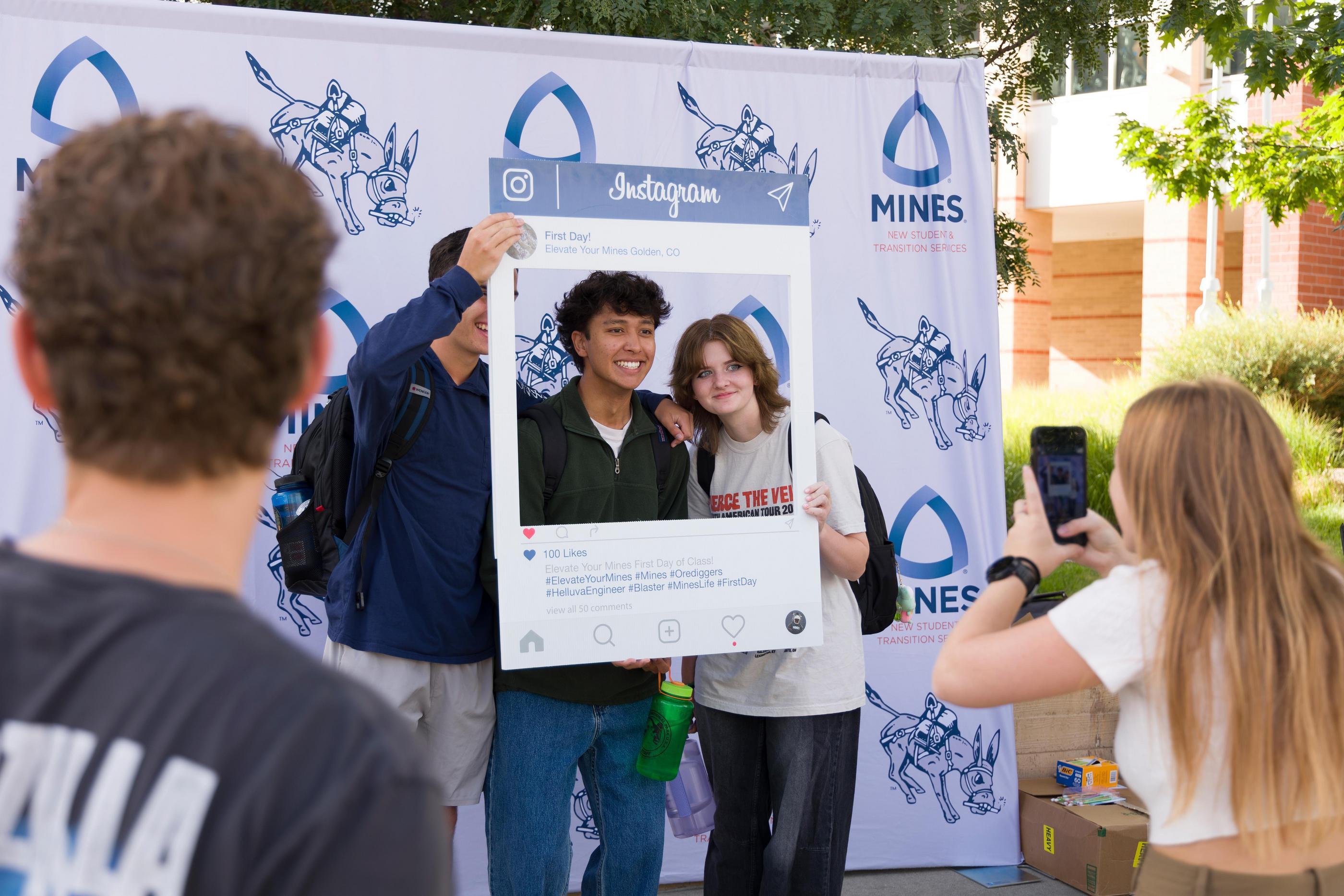 Three students pose with an oversize Instagram photo frame prop