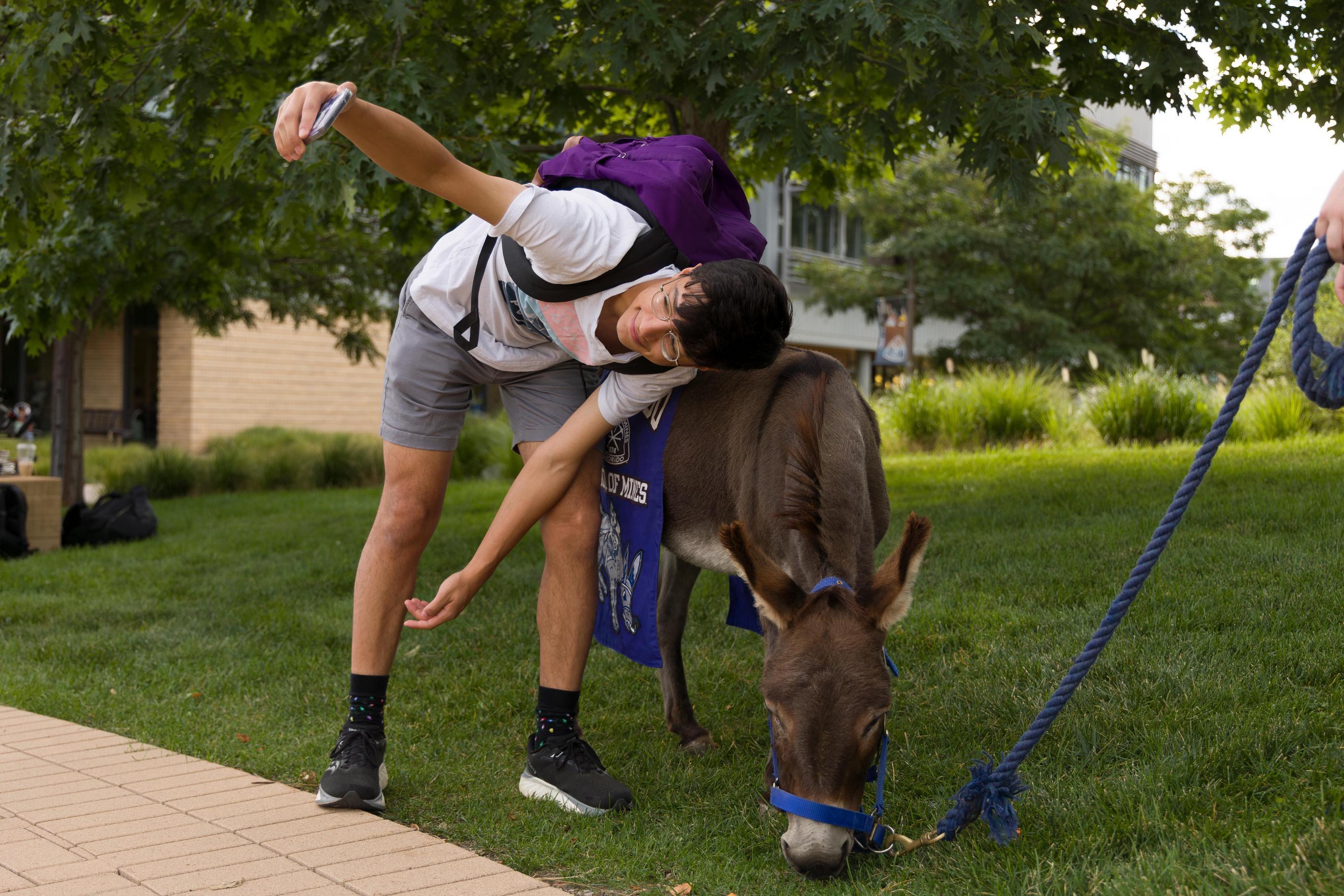 Student wearing a purple backpack poses for a selfie with Blaster the burro