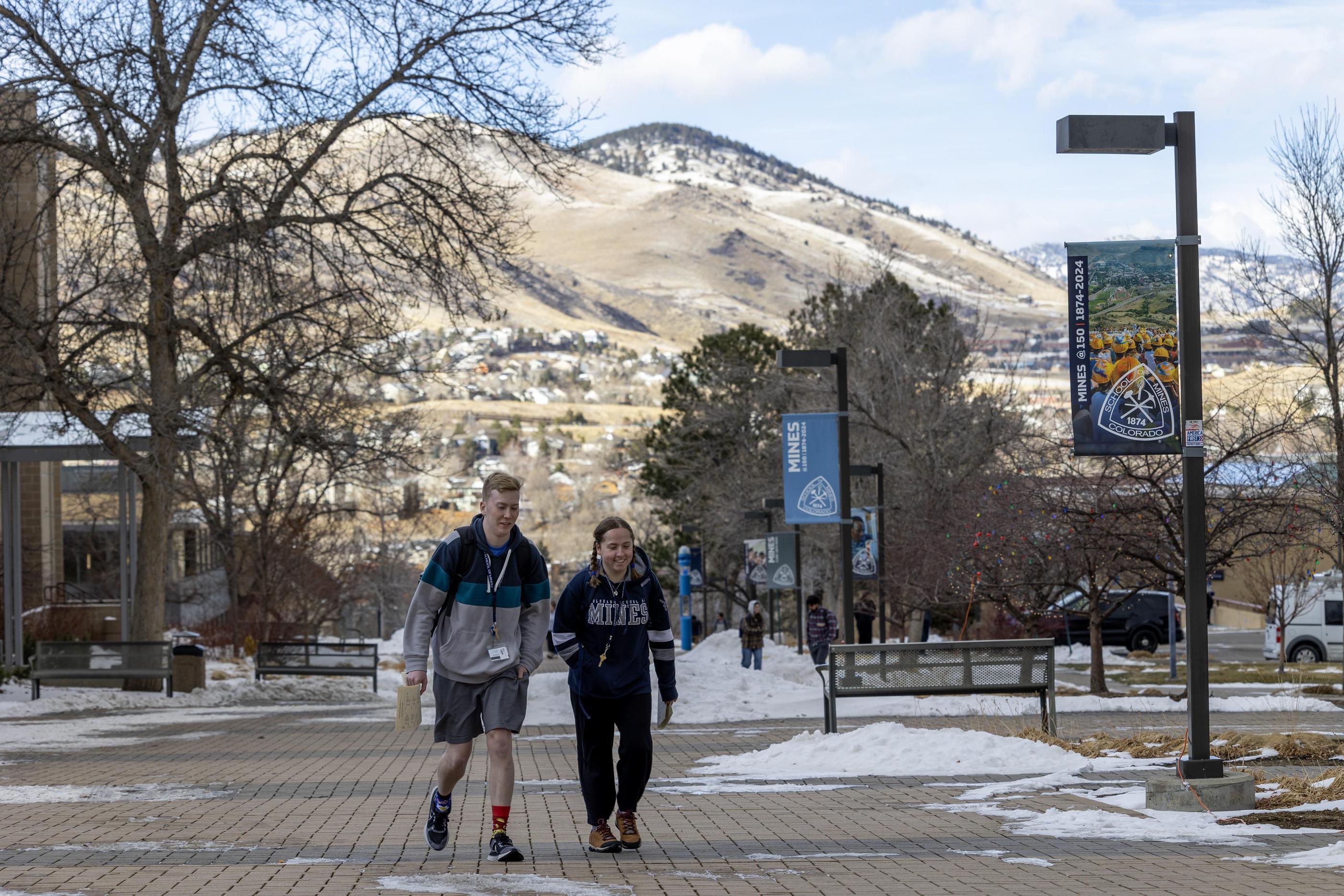 Two students walk down the pedestrian plaza with piled snow