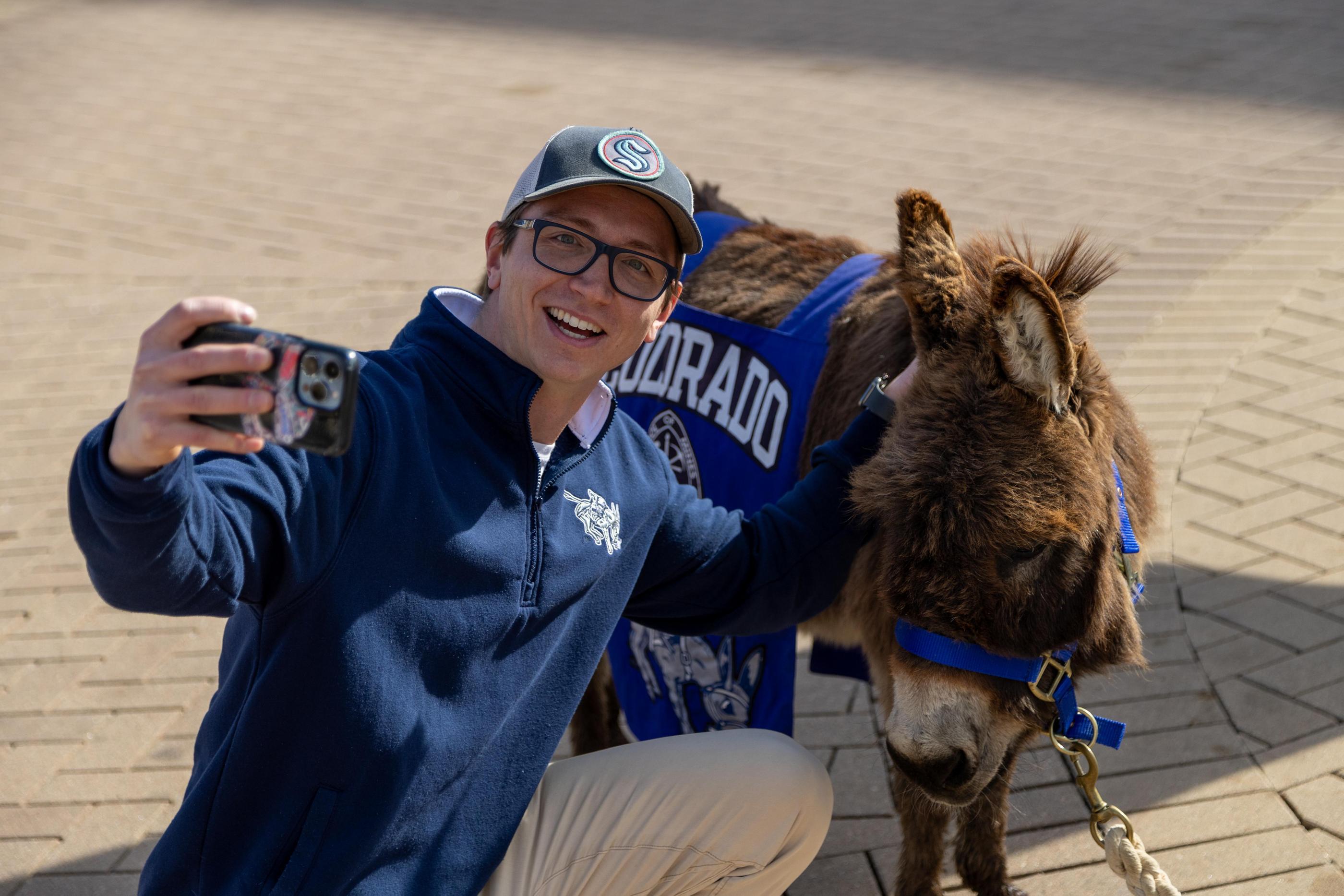 A person in Mines gear poses for a selfie with Blaster the burro