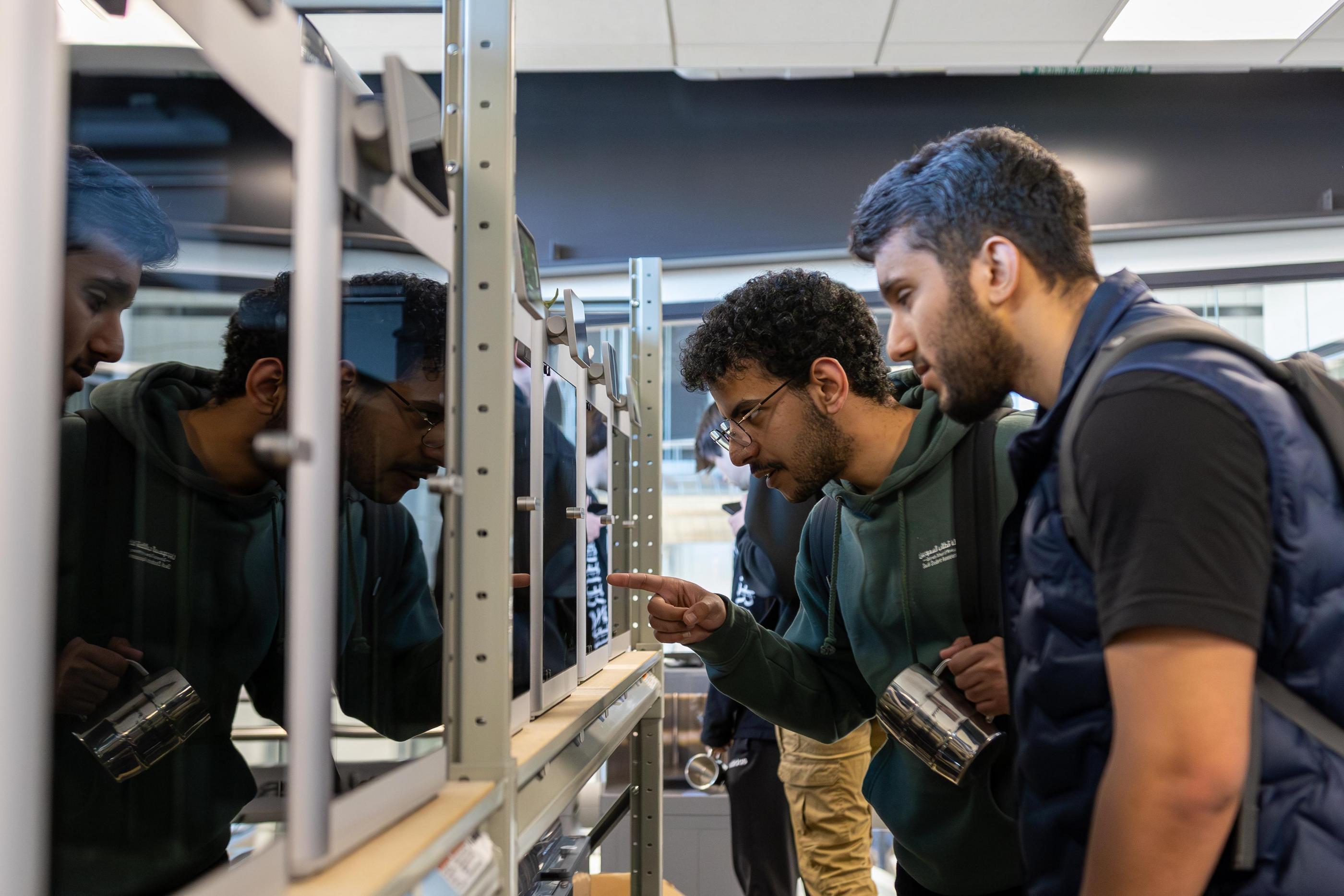 Two students look at a 3D printer at work