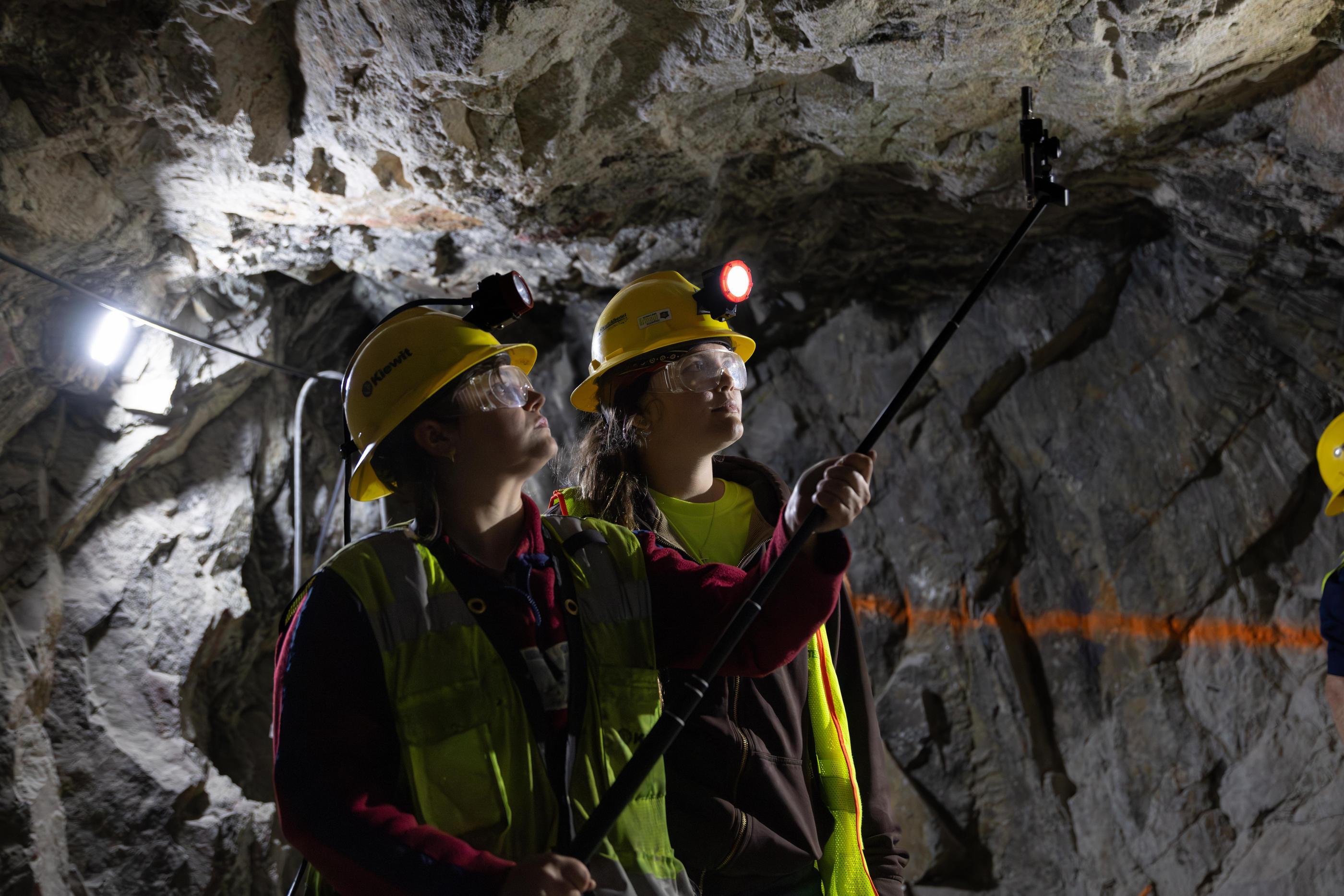 Two students in hard hats and safety glasses use a pole-mounted scanner to survey a rock face inside the Edgar Experimental Mine during a Colorado School of Mines geology field session.