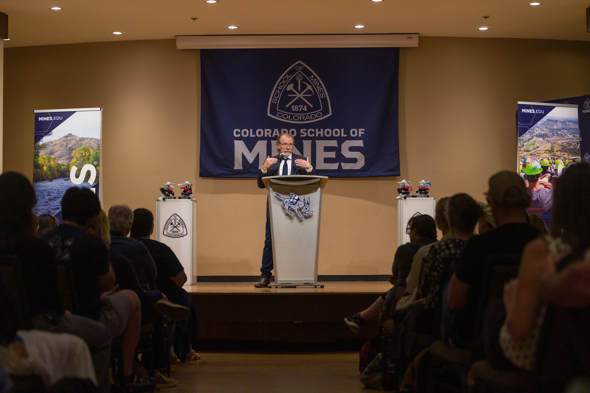 George Saunders standing at lectern in front of Mines flag and audience