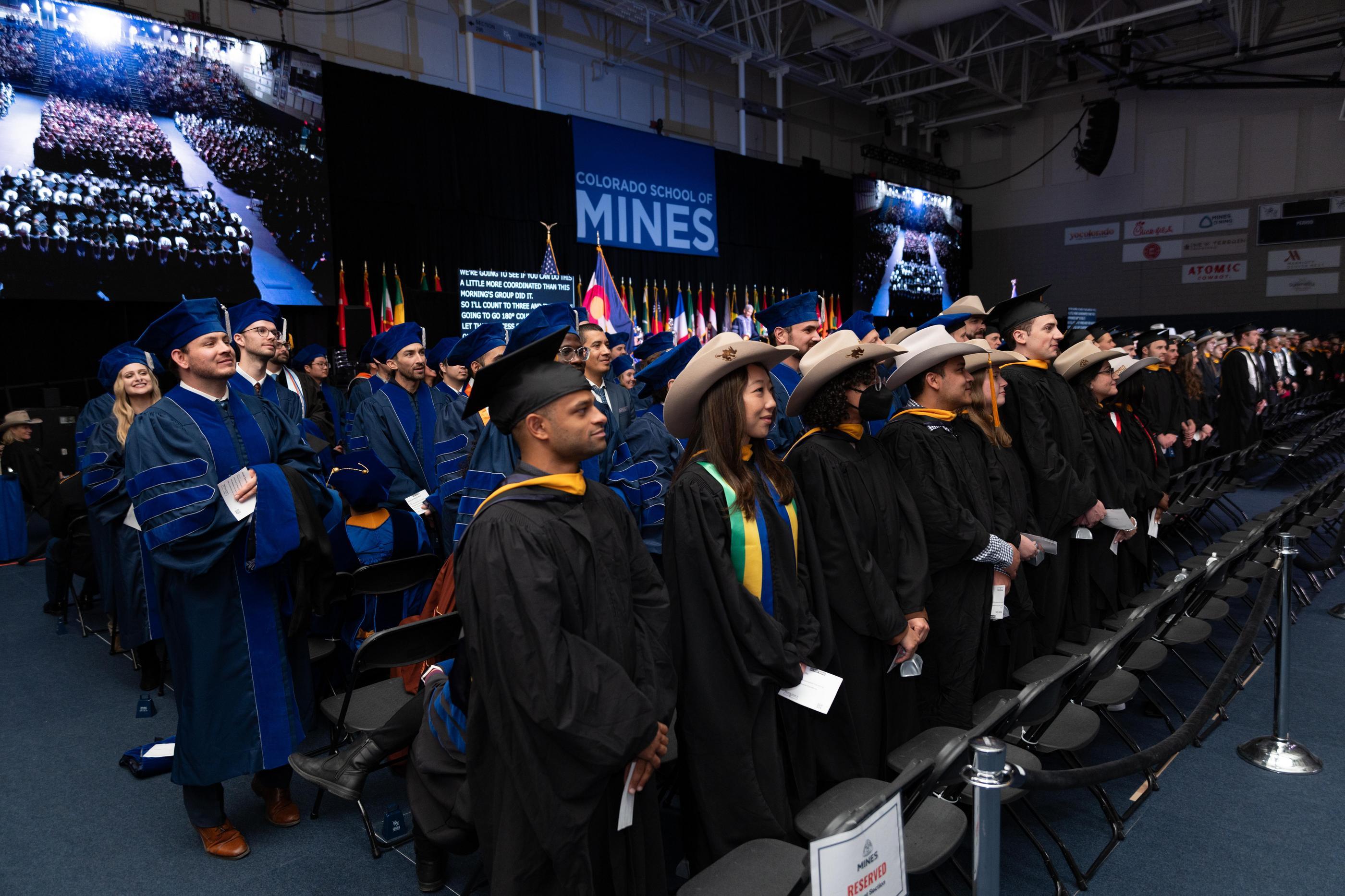 Mines graduate students in academic regalia, including caps and gowns, stand together during commencement, with the 
