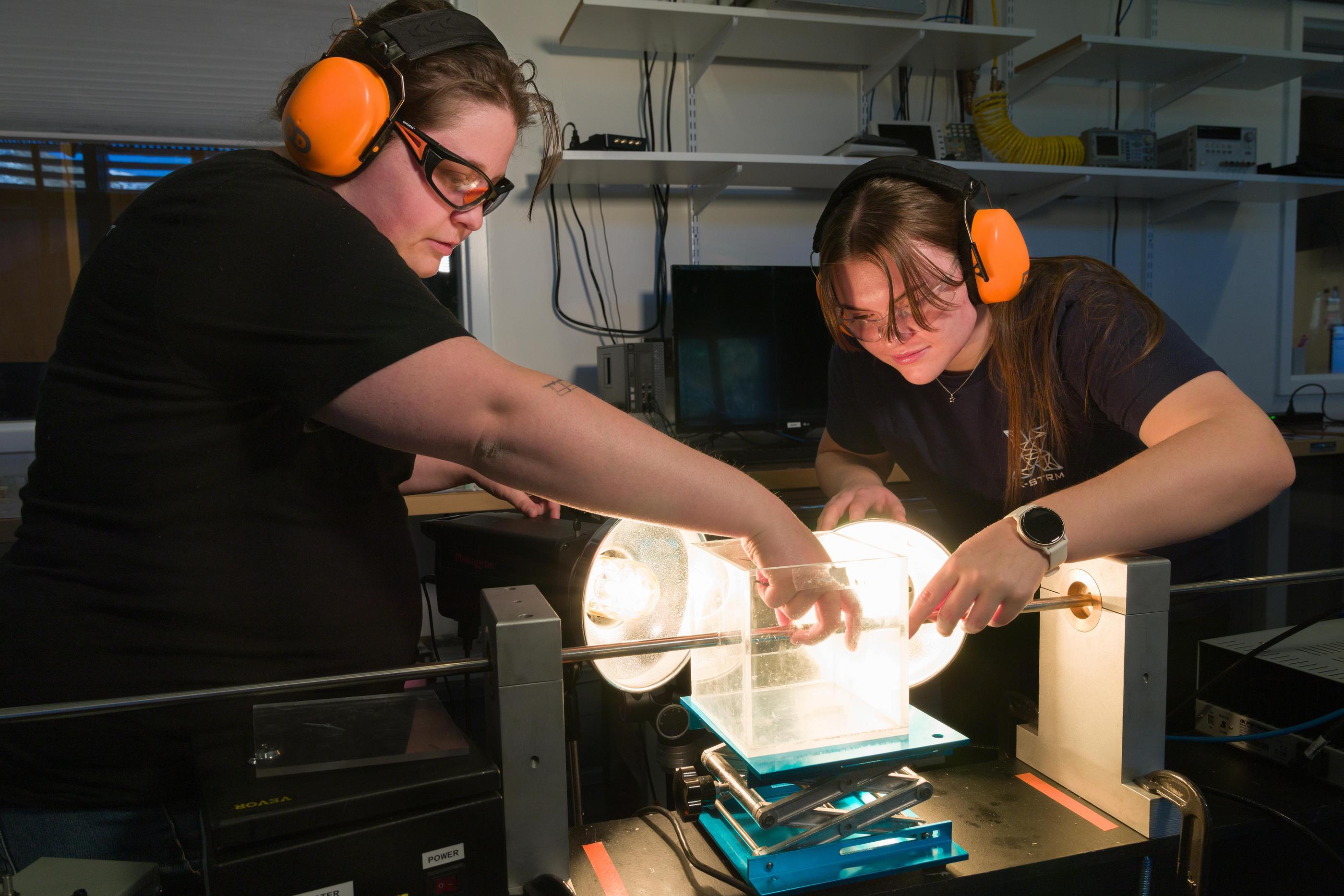 Two students wearing orange protective earmuffs work on experiment in materials lab