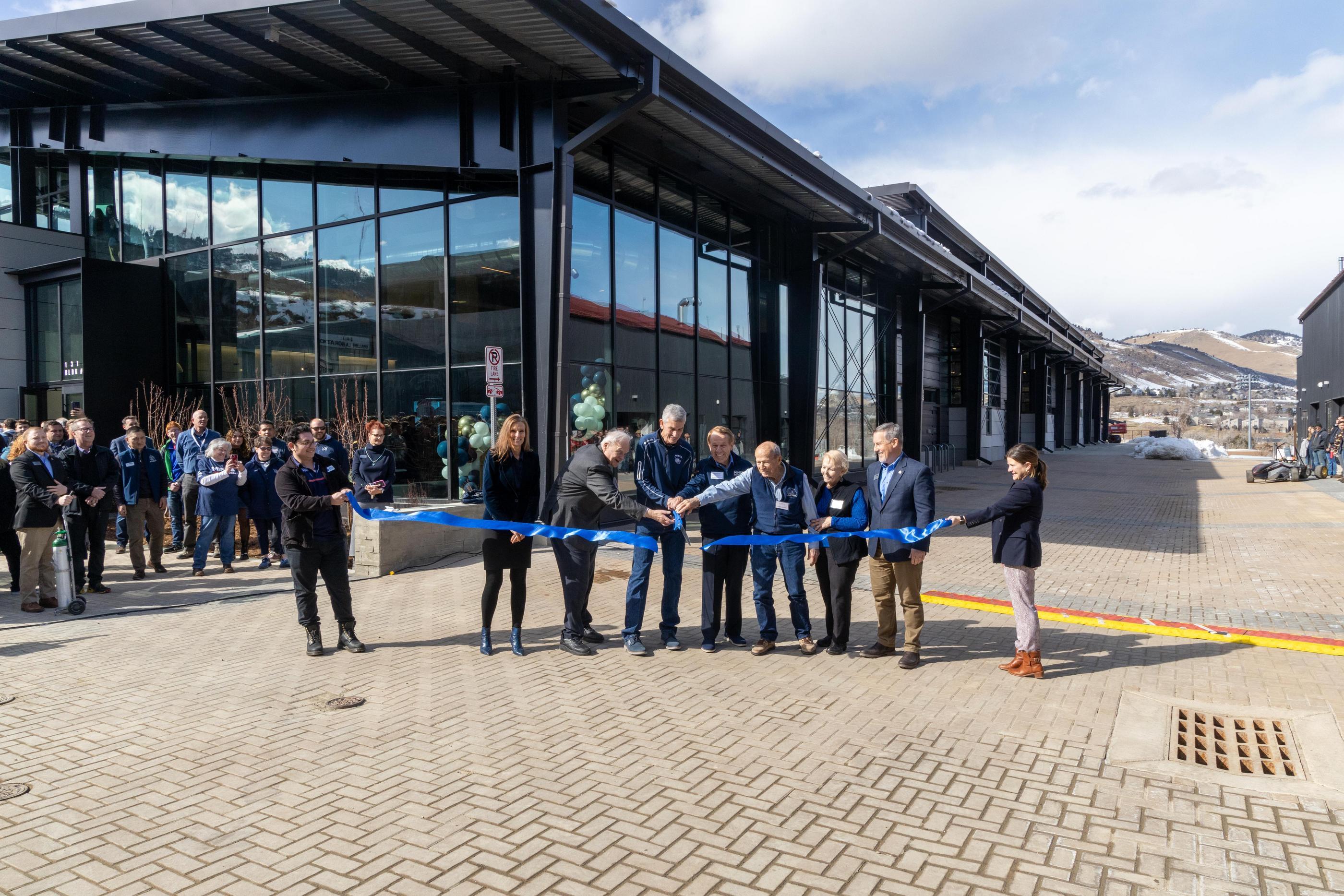 A line of people stand behind a giant blue ribbon being cut