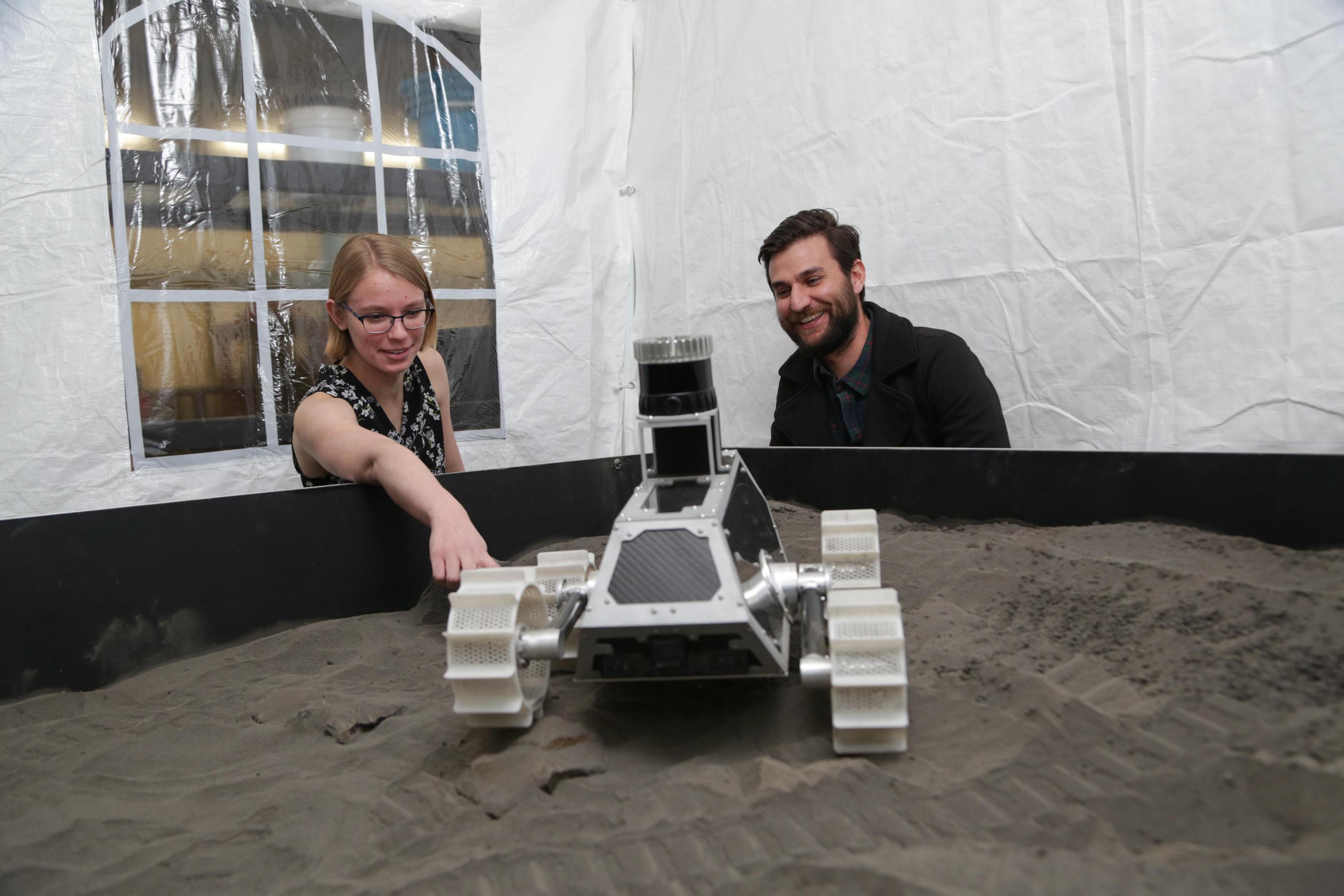 A student points at a Lunar Outpost rover being tested in simulated lunar soil