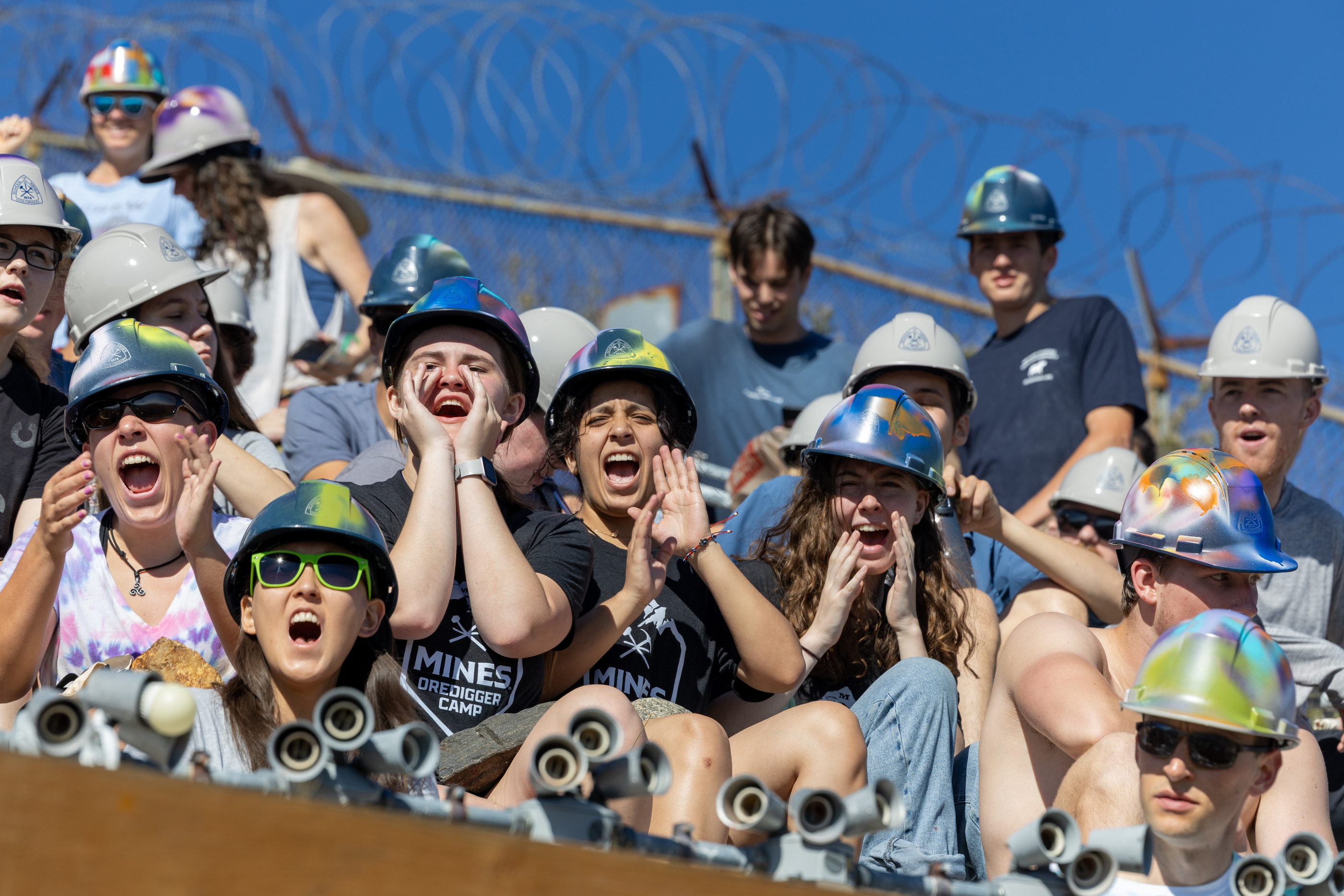 Students wearing hard hats sit on the M and cheer
