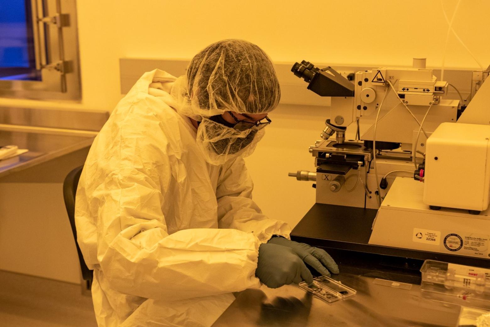 A Colorado School of Mines student wearing a white lab suit with safety glasses and gloves performs an experiment at the Quantum Lab.