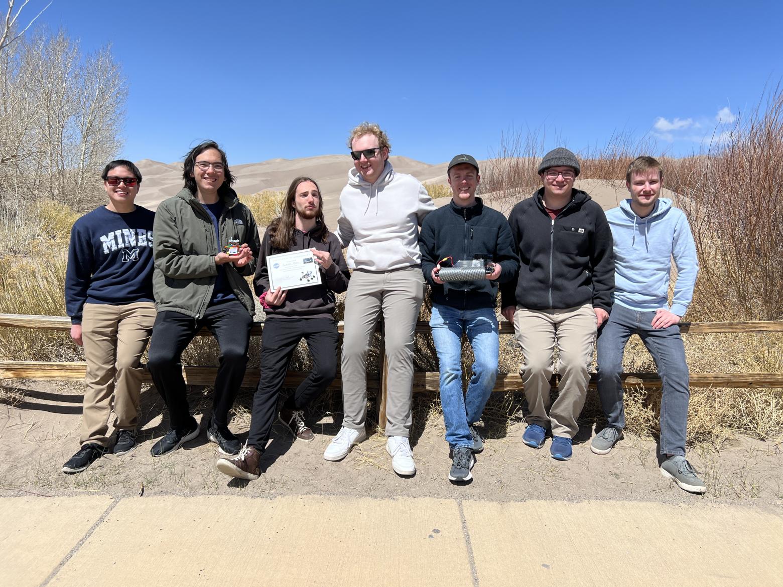 Group of Mines students sitting on a wooden fence railing with Great Sand Dunes in background