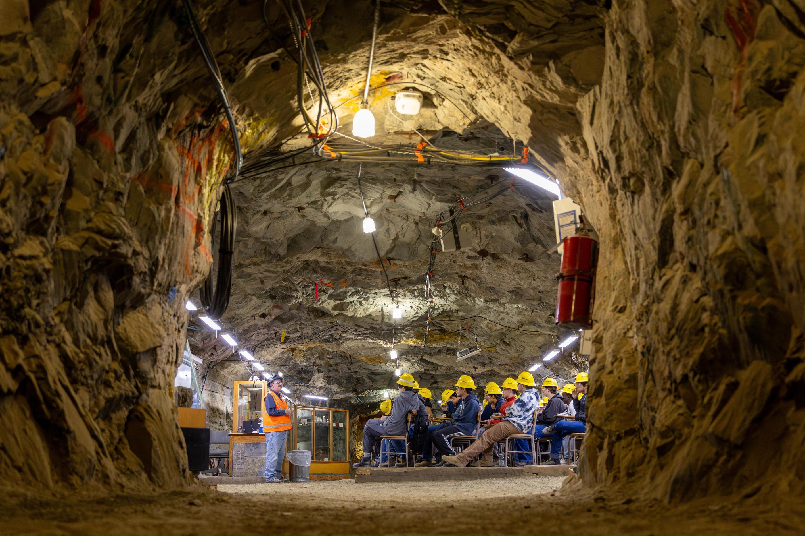 Students in yellow hard hats sit at desks in a classroom hewn out of a mine