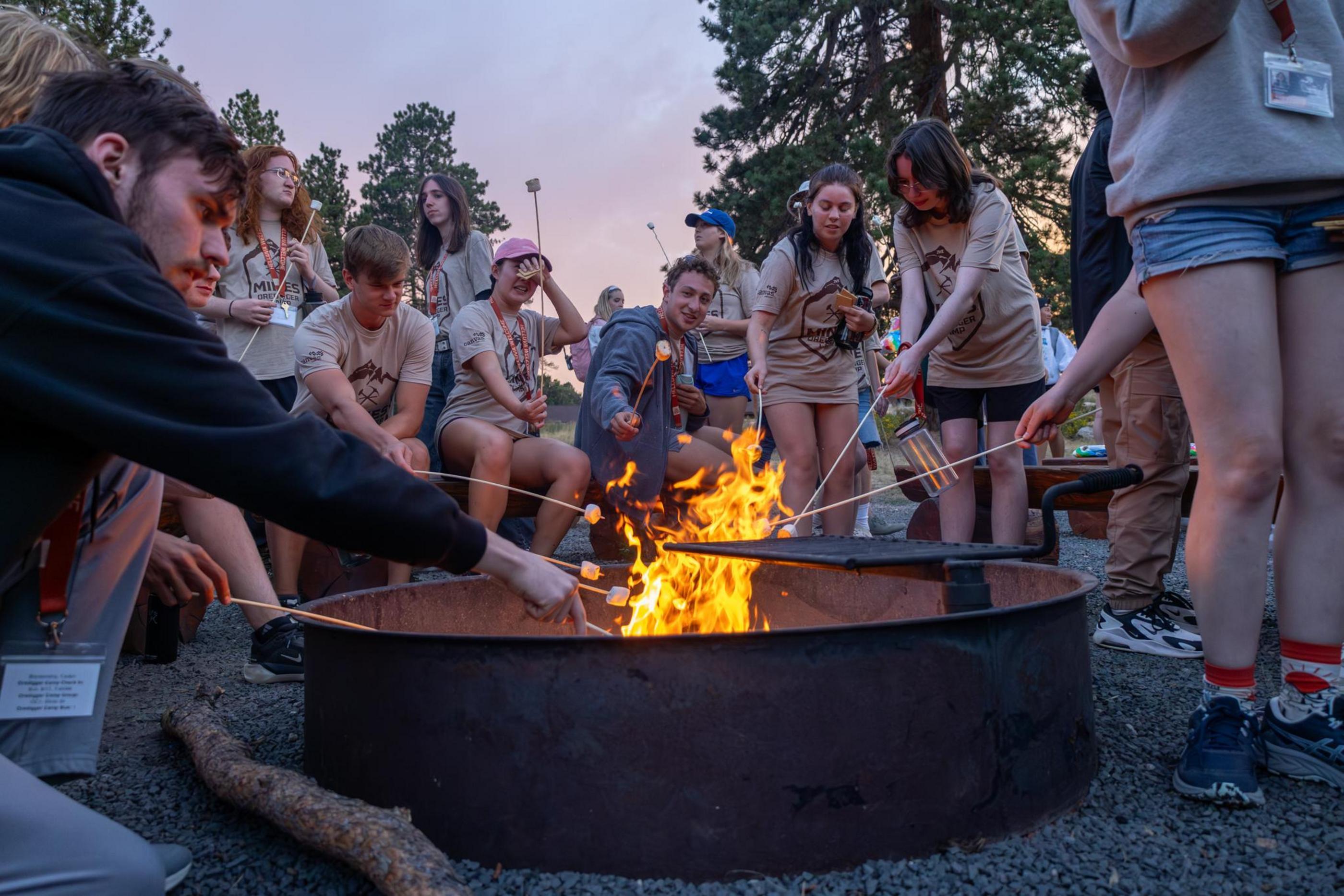 Students stand around a fire pit roasting marshmallows