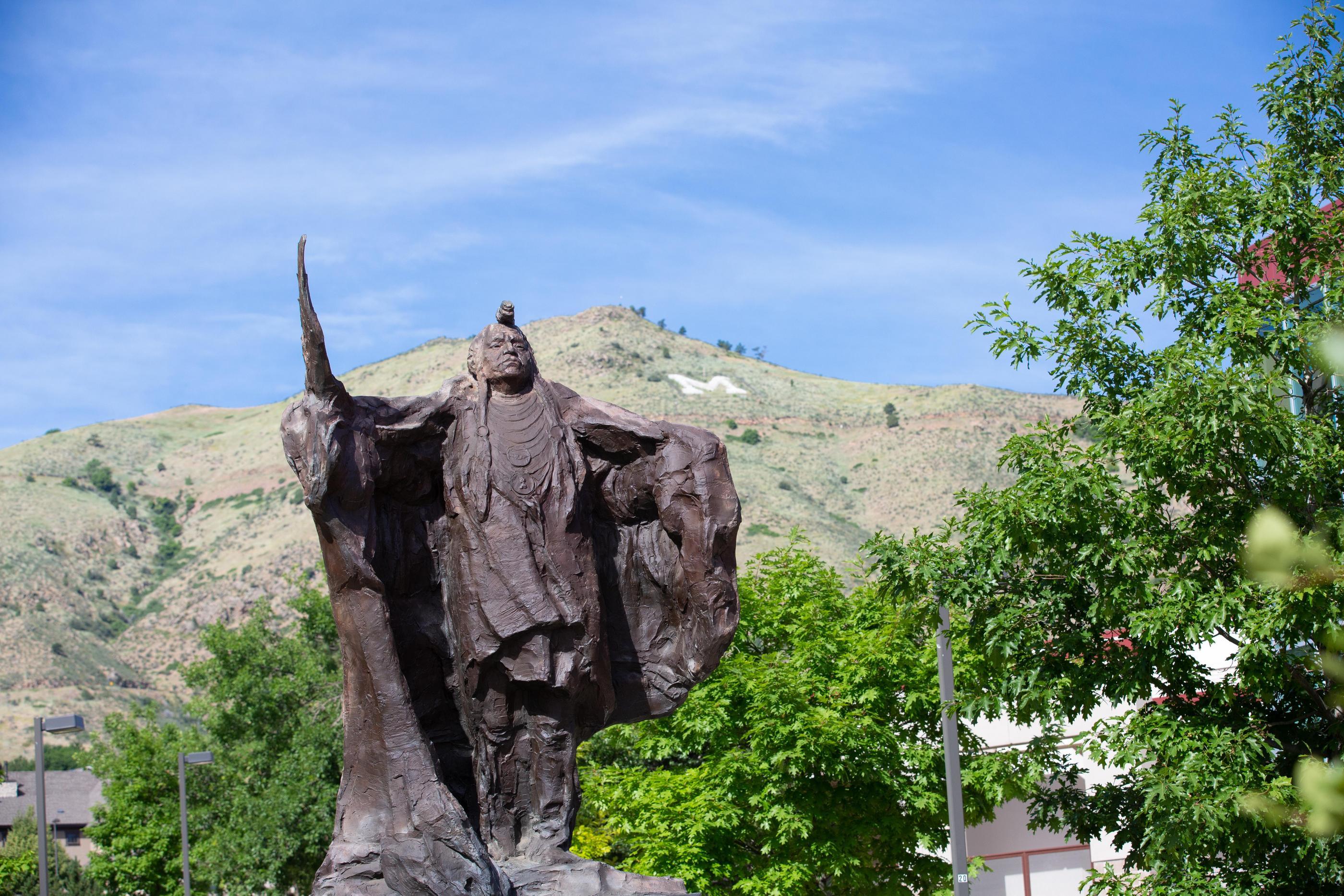 A statue of a Native American with the hillside M in the background
