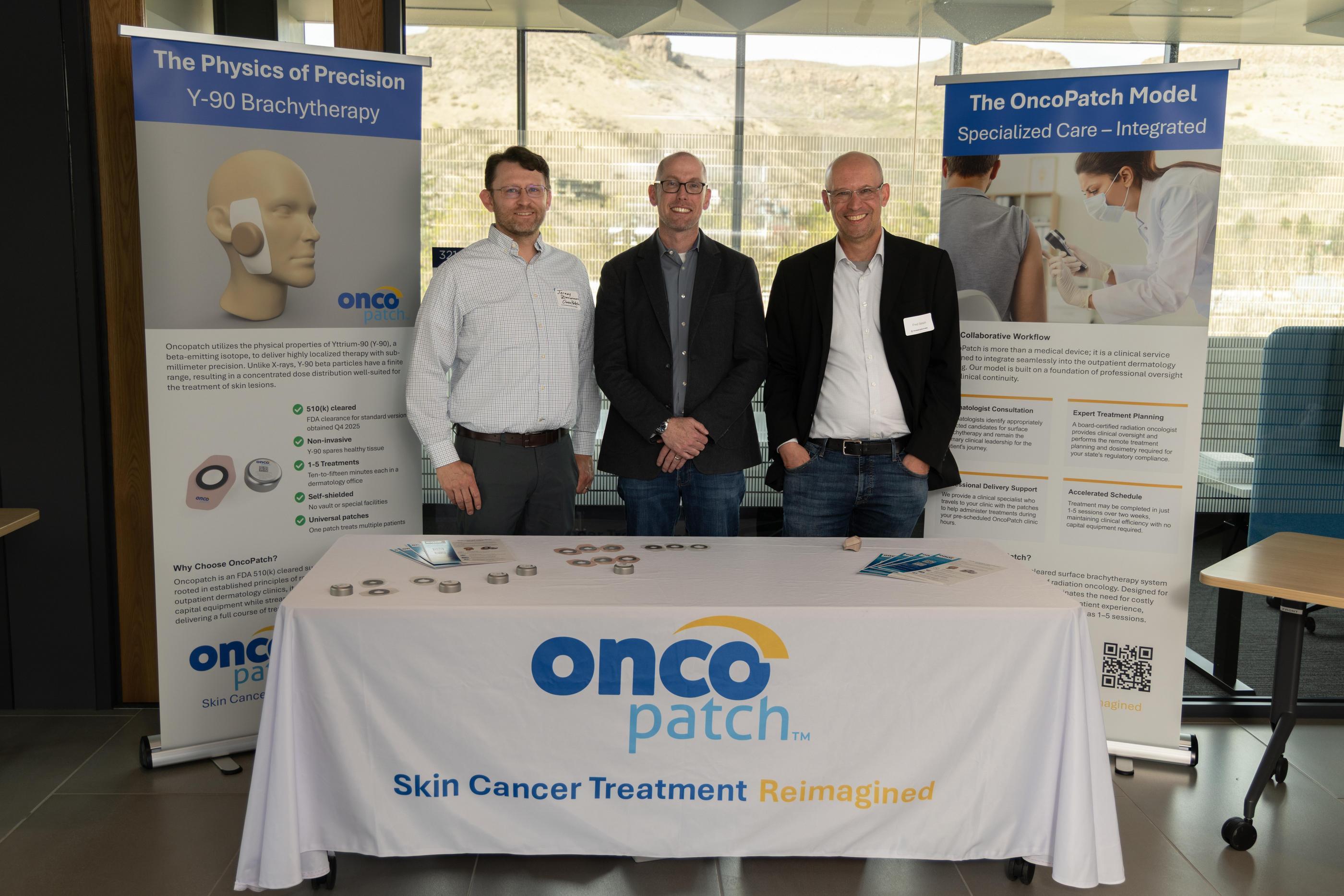 Three co-founders of OncoPatch stand at a booth
