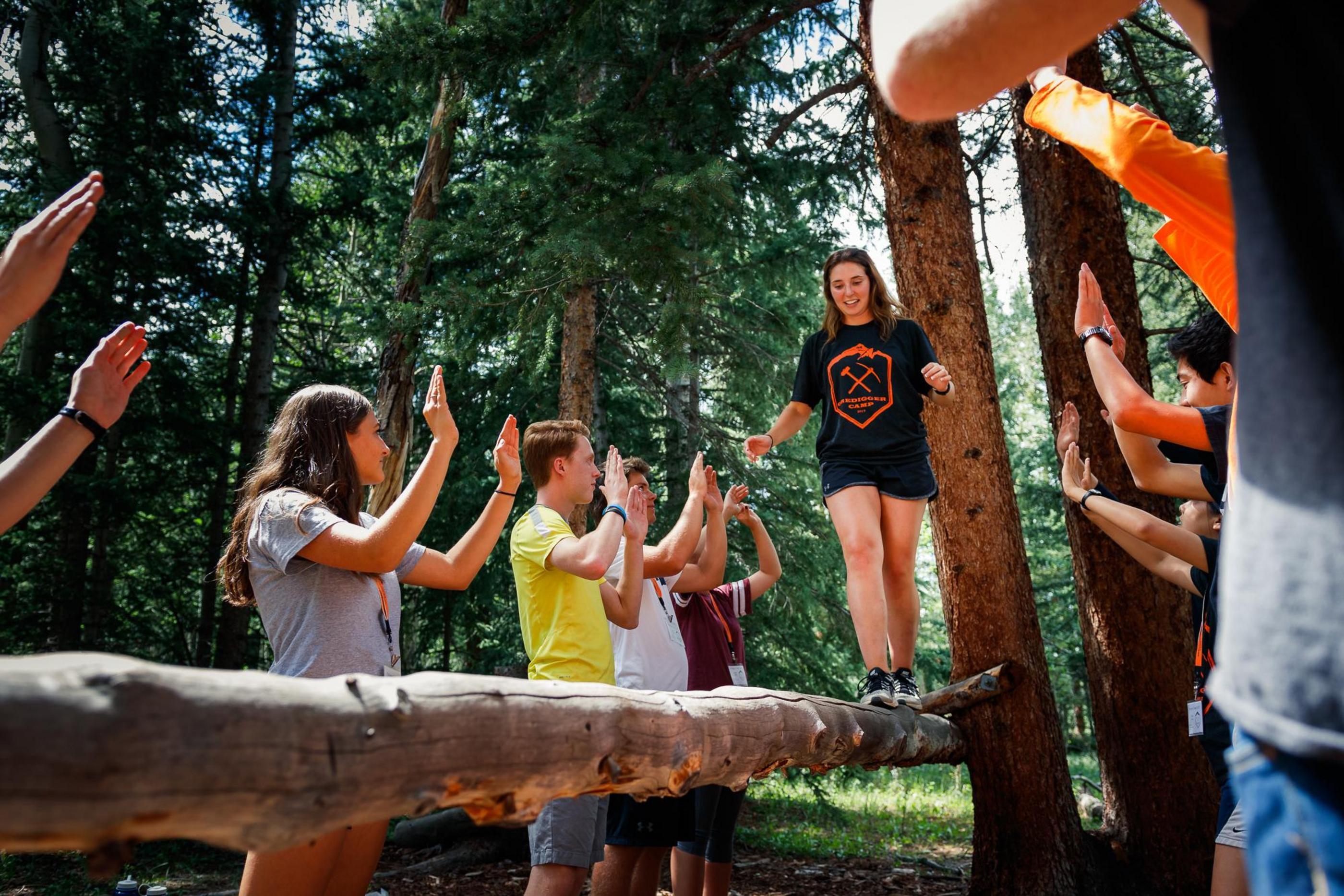 Student walks across a log balance beam with other students lining each side with hands up