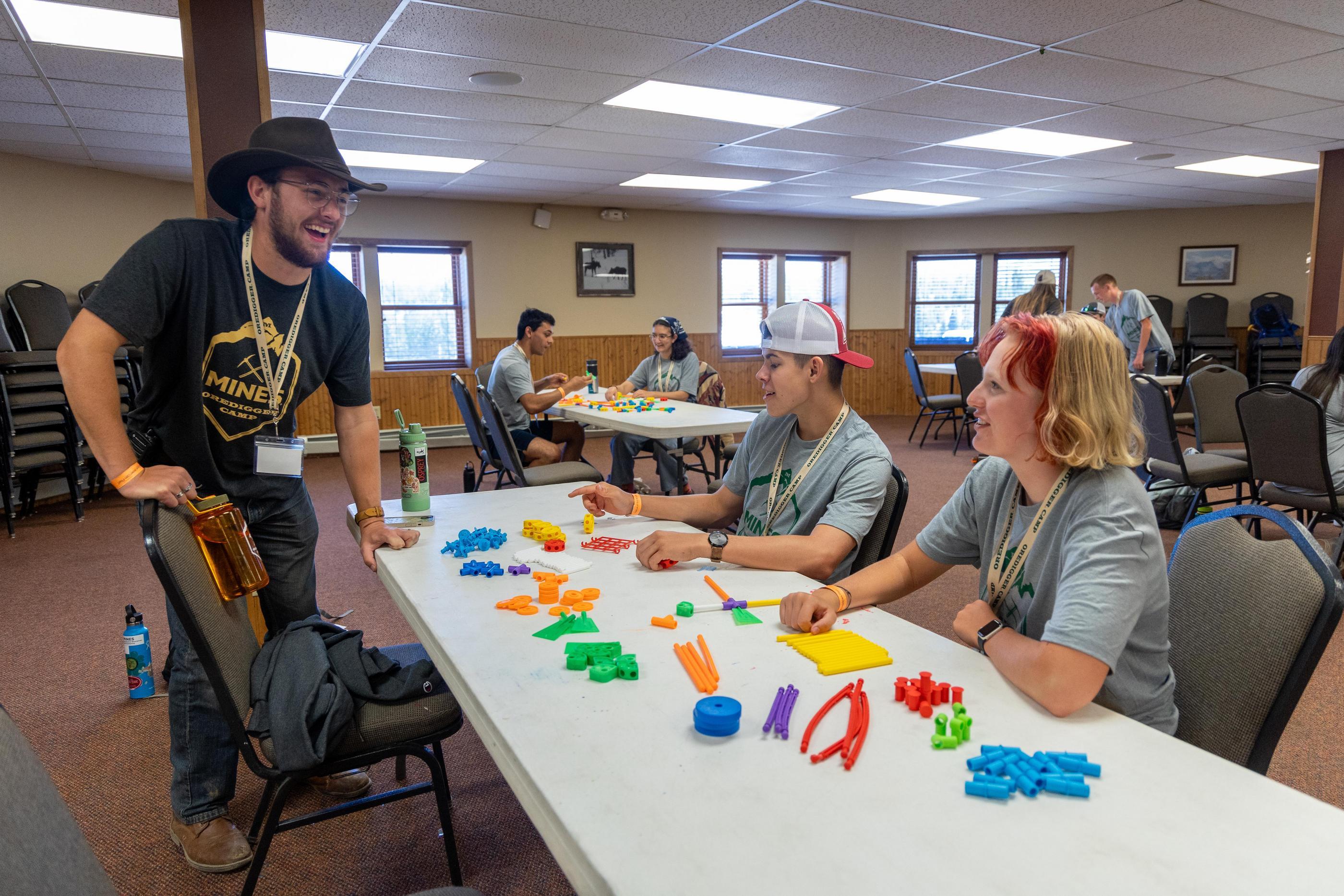 Two students sit at a table covered in colorful plastic pieces during an engineering challenge