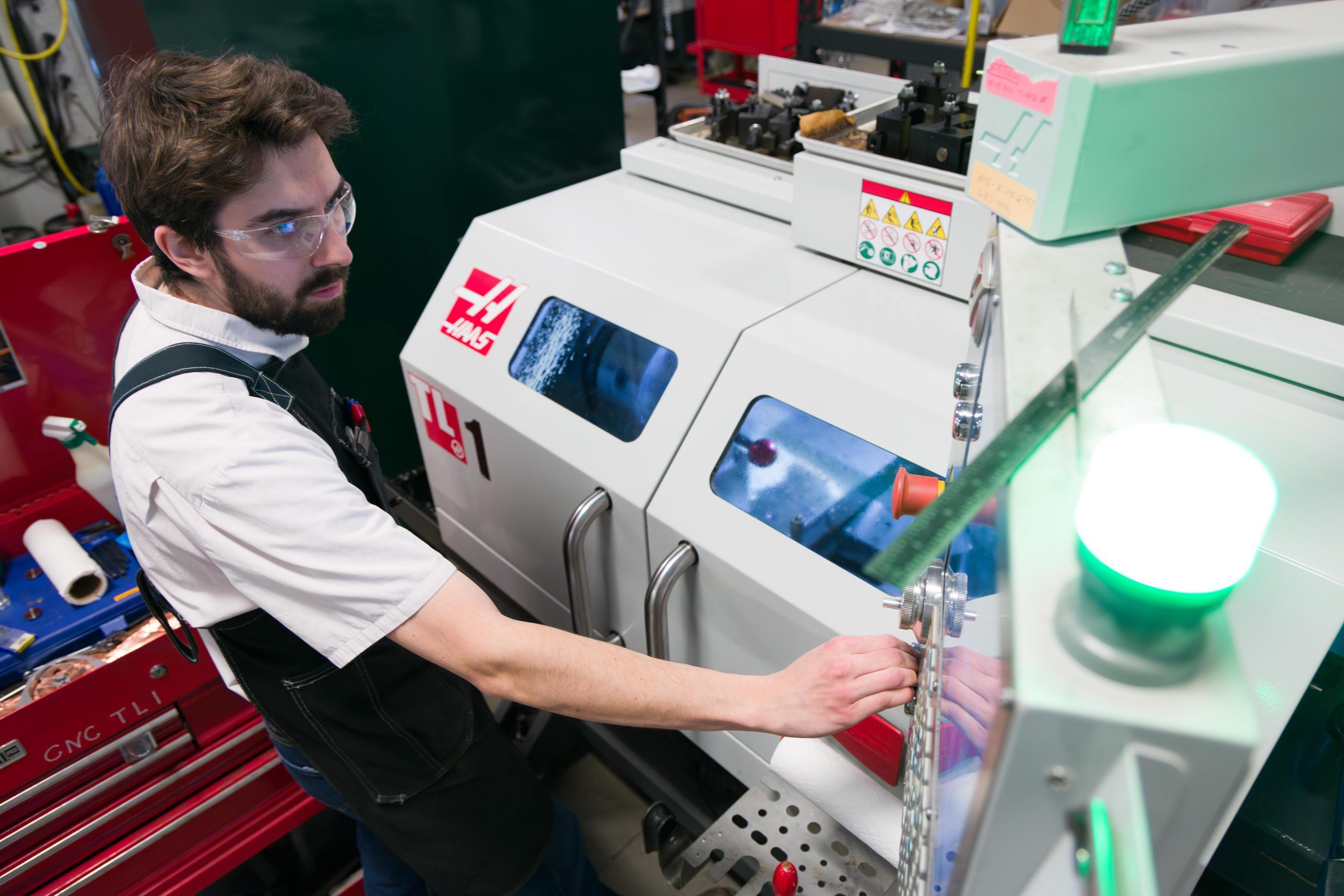 A man in safety glasses and apron works in machine shop