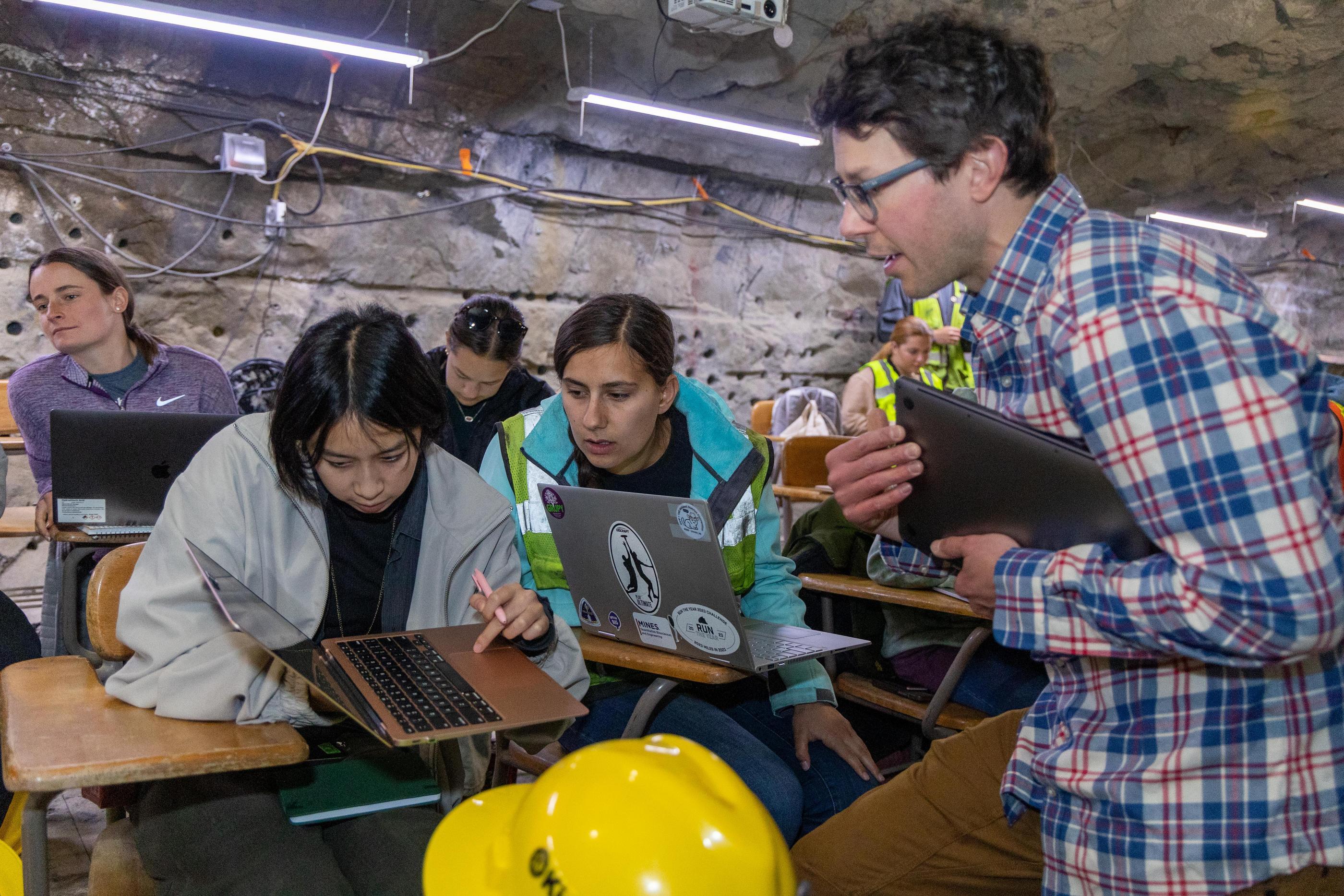 A professor and two students look at a laptop screen in the underground classroom at Edgar Mine