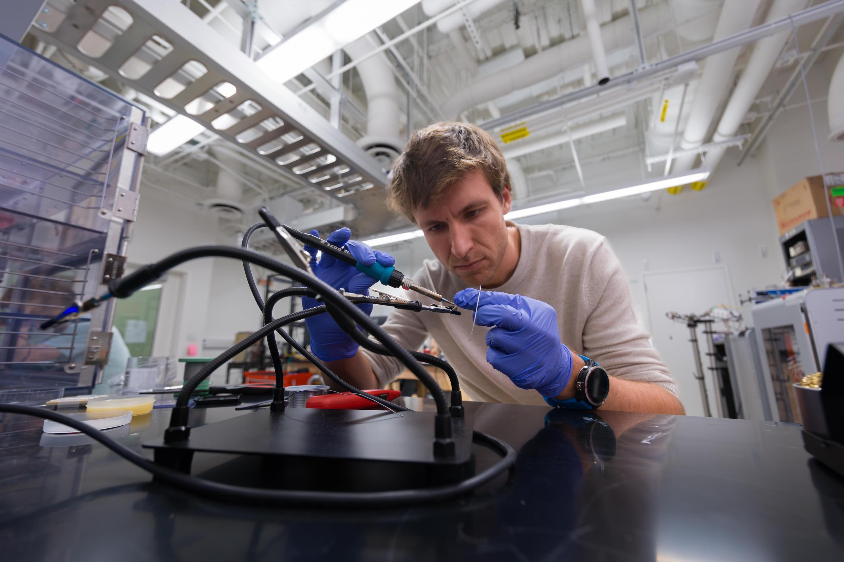 Wouter Van De Pontseele wearing blue gloves carefully assembling wiring for cryogenic equipment.