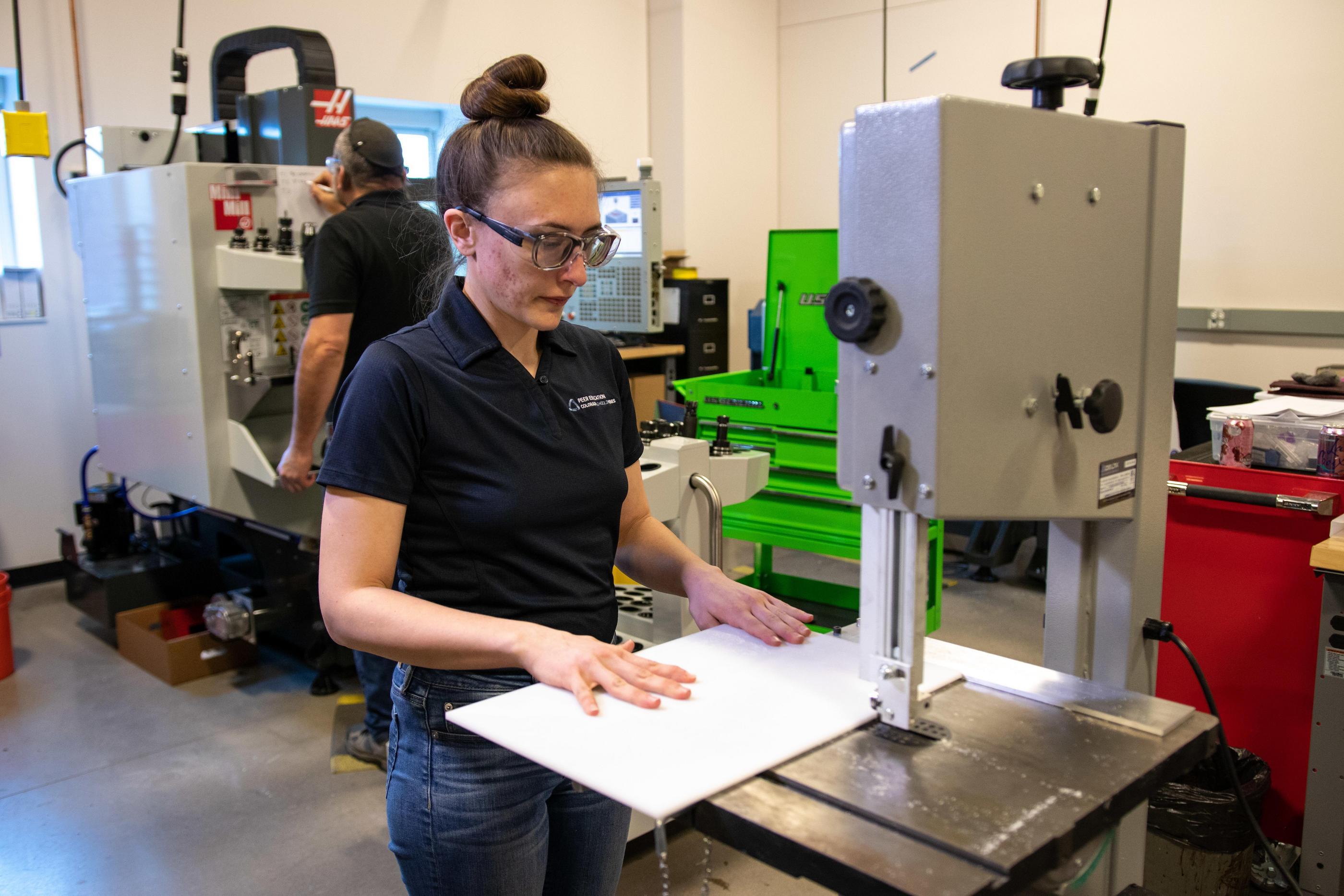 A female student in a blue polo shirt works in the machine shop