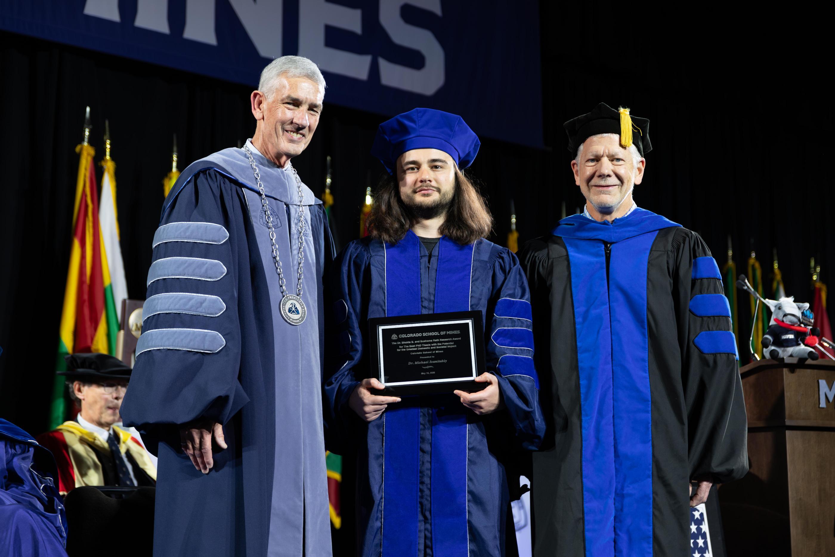 PhD grad holds award on commencement stage between Mines President and Interim VPR