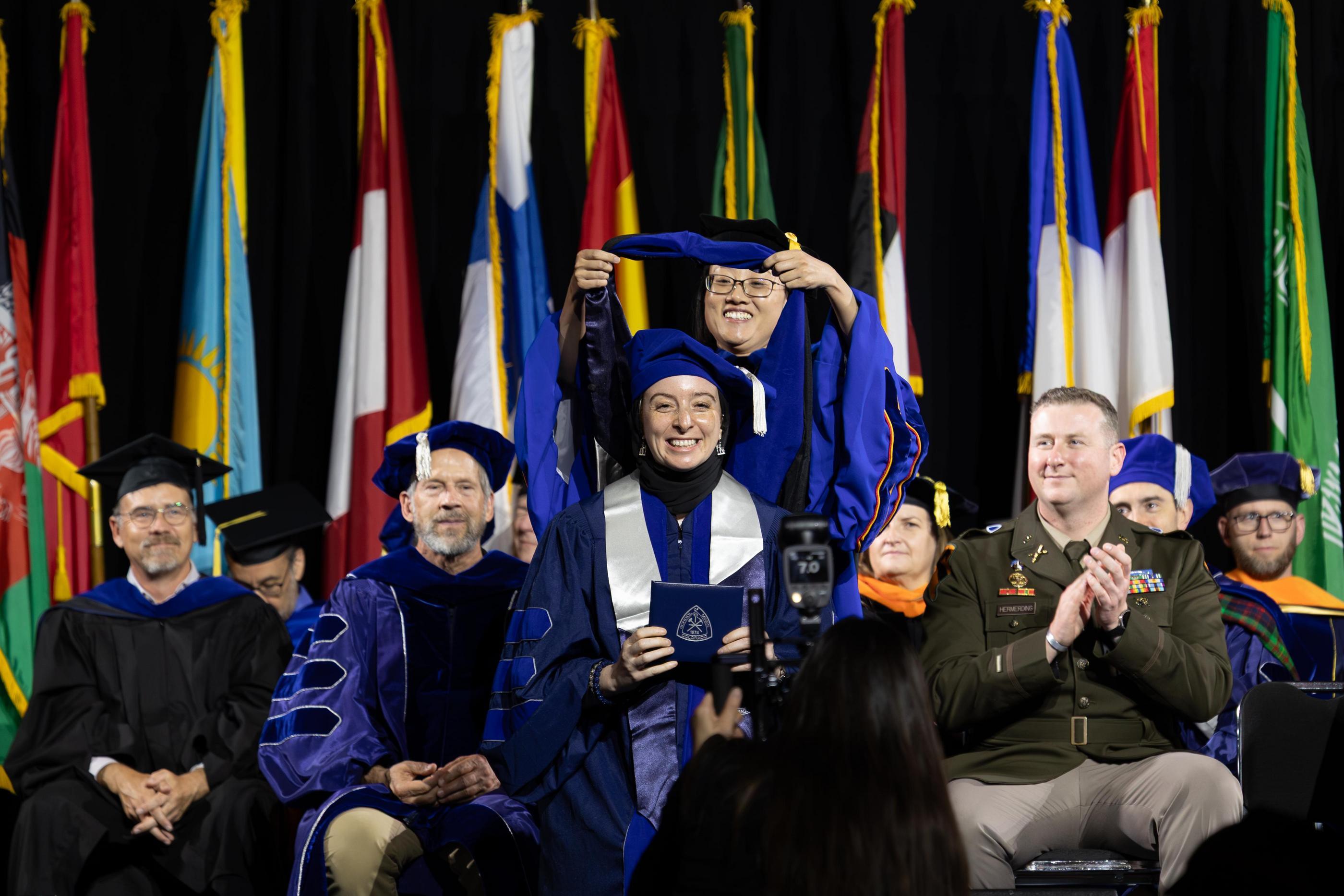A PhD graduate is hooded on stage during Colorado School of Mines Spring Commencement