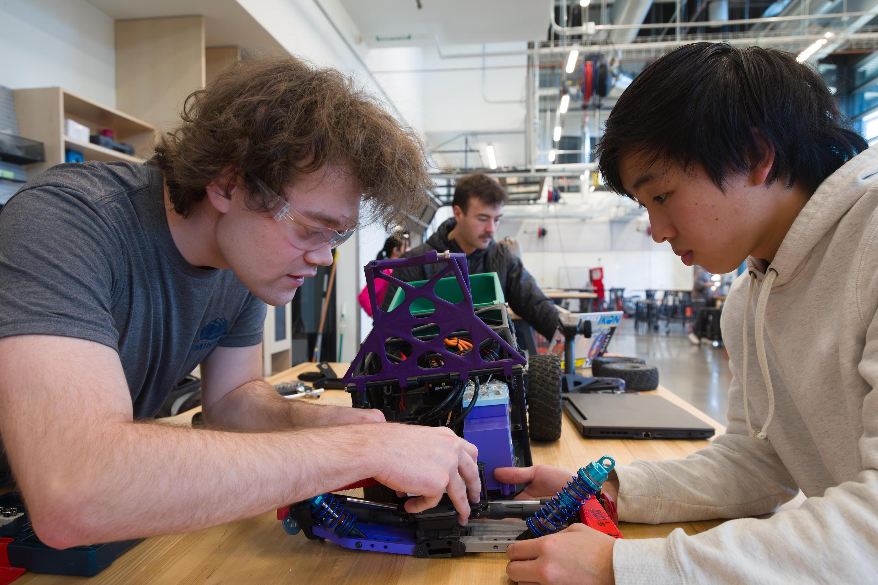 Two male students work on a RC car part at a work bench