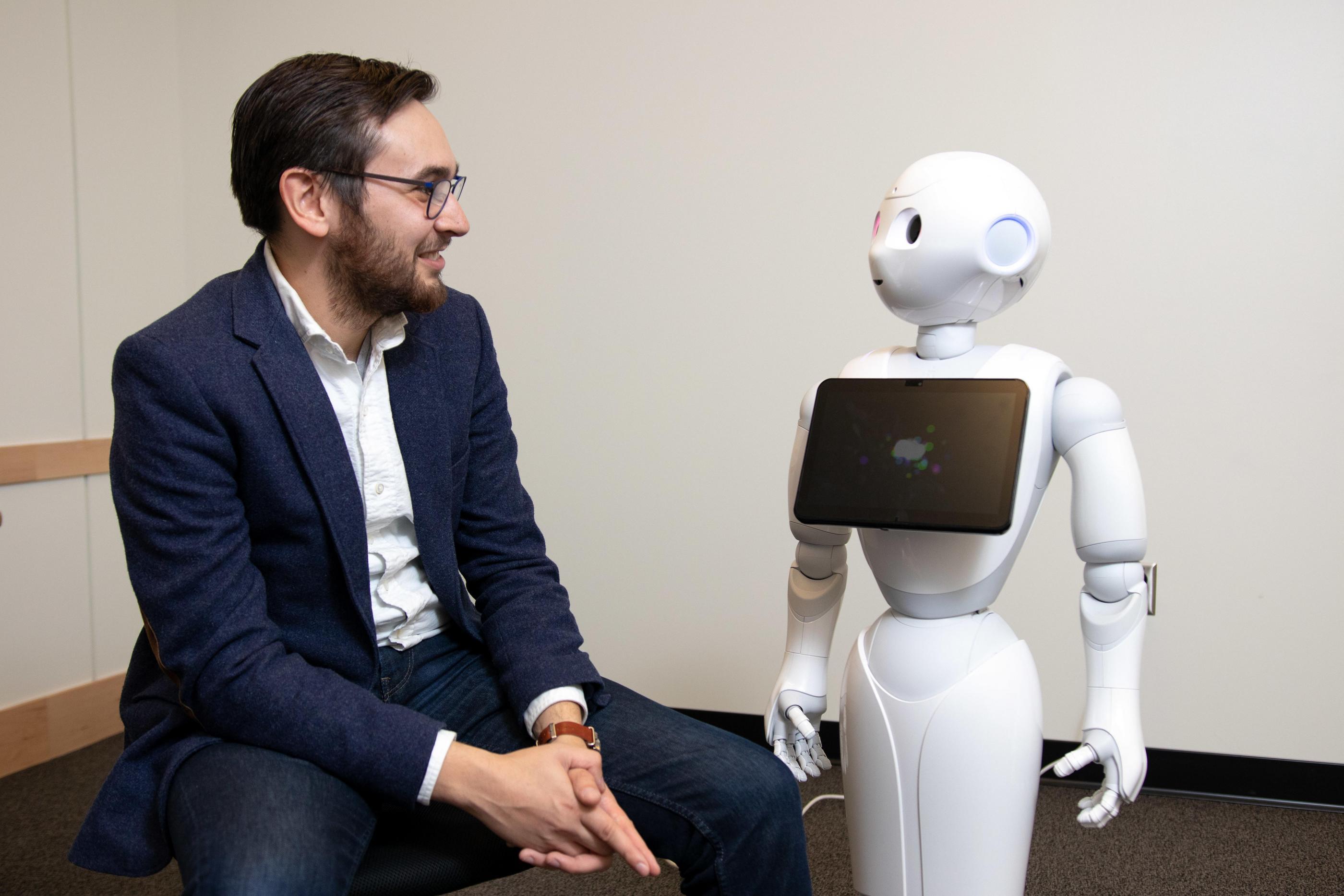 Tom Williams sits next to a white humanoid robot