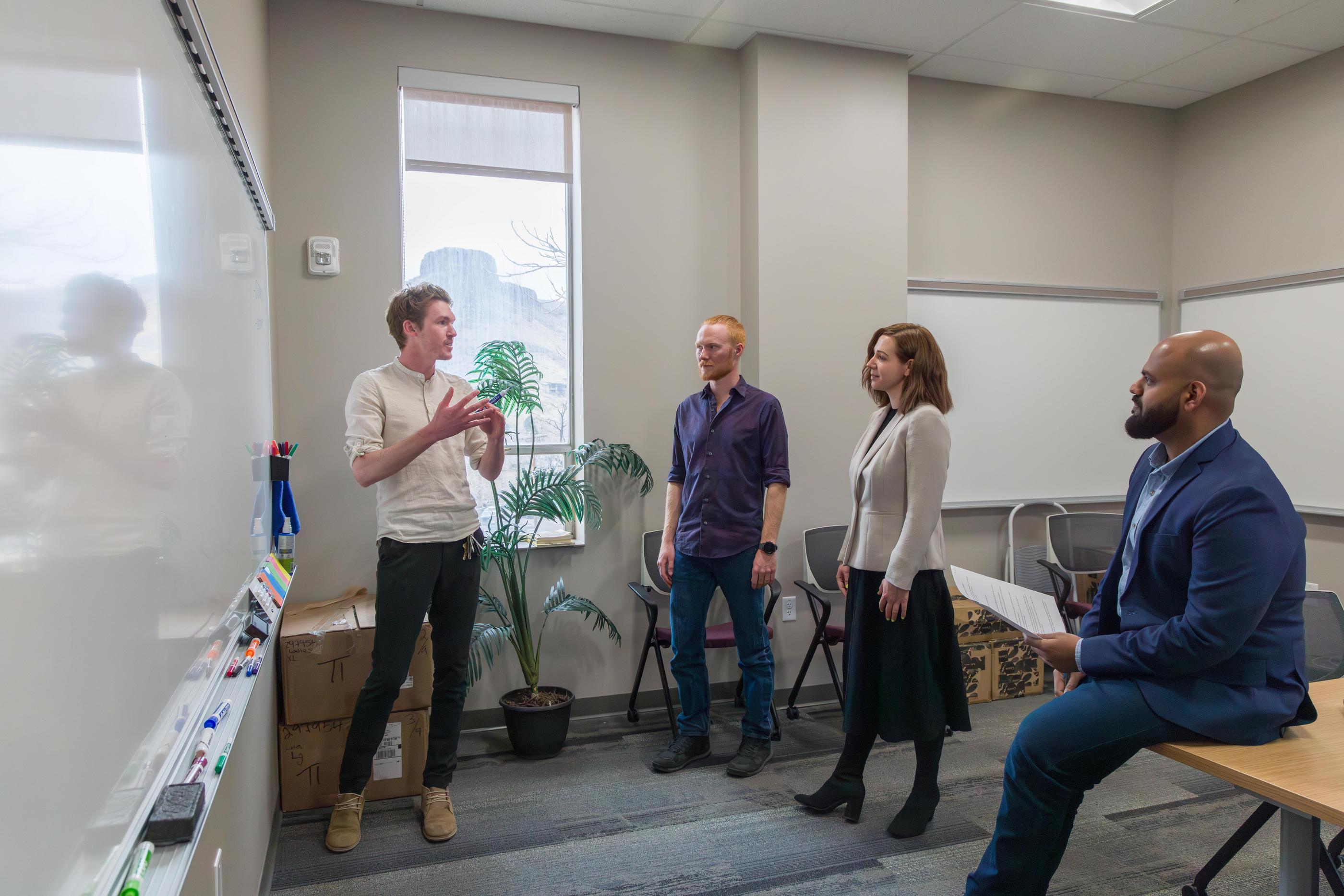 A group of standing faculty members talk in front of a white board