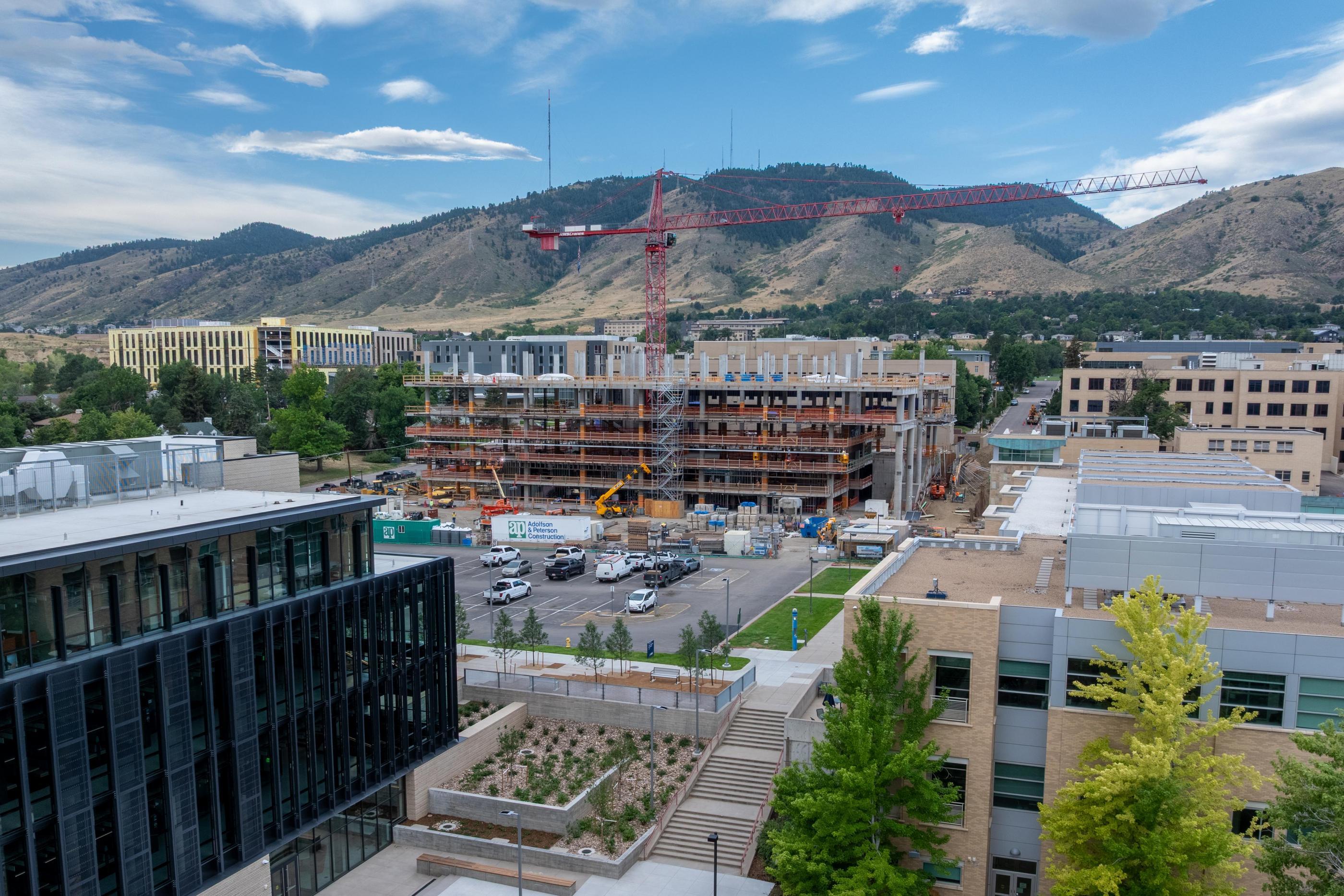 Aerial view of the Energy and Minerals Research Facility under construction on the Colorado School of Mines campus in Golden, Colorado, with a tower crane rising above the steel-framed building and the foothills in the background.