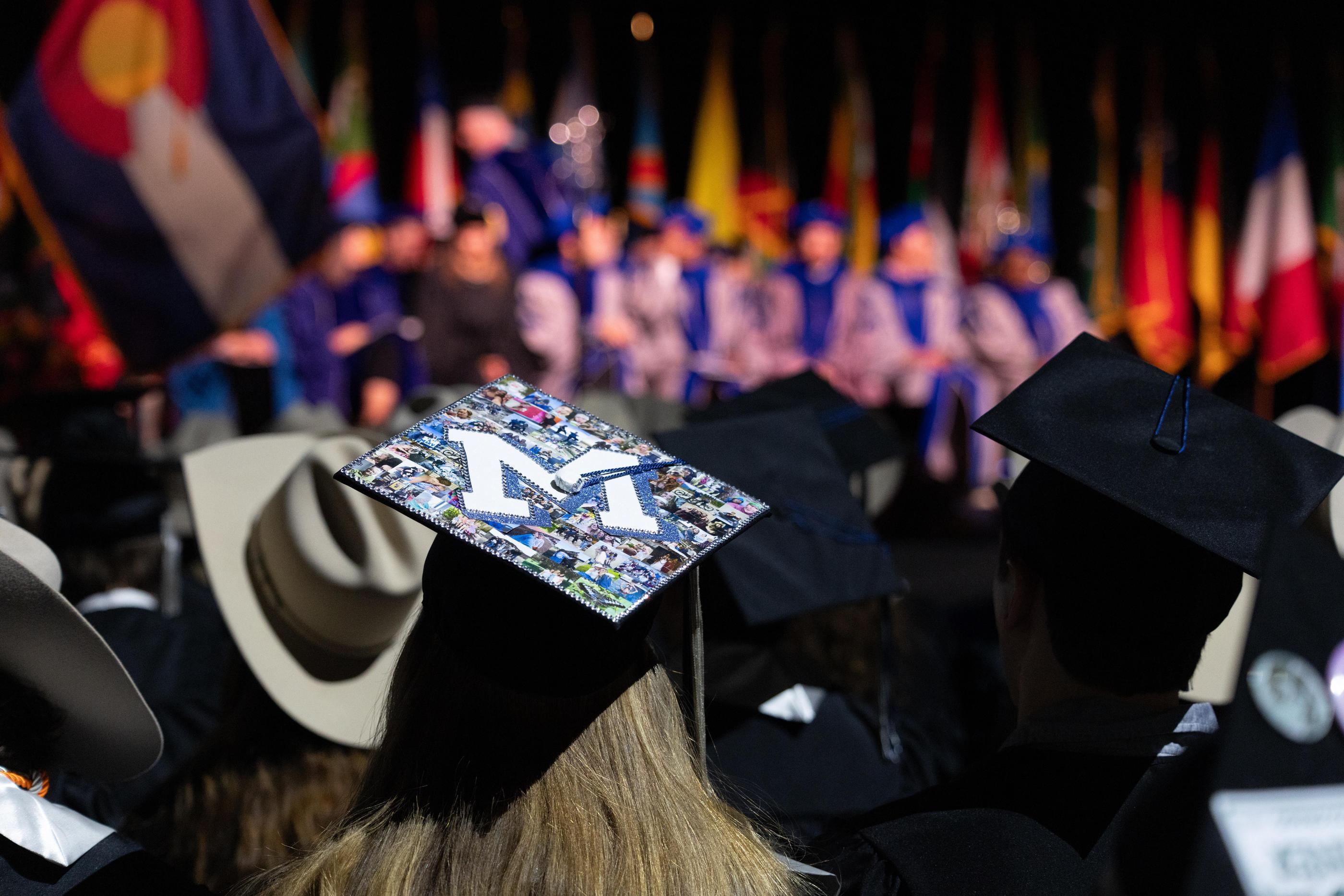 A student wears a mortarboard decorated with Mines M sitting with other graduates at commencement