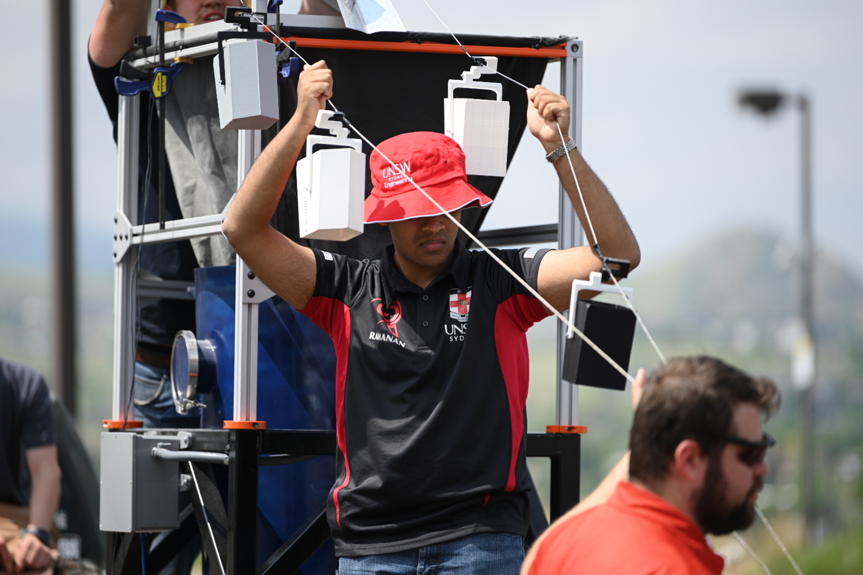 A student in a red bucket hat adjusts a conveyance system for regolith