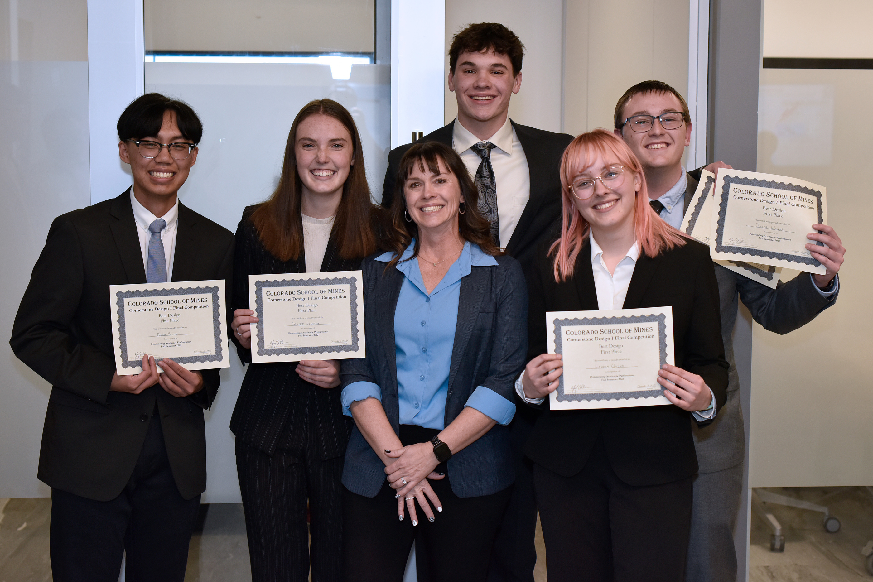 Five students in business wear holding certificates pose around their advisor