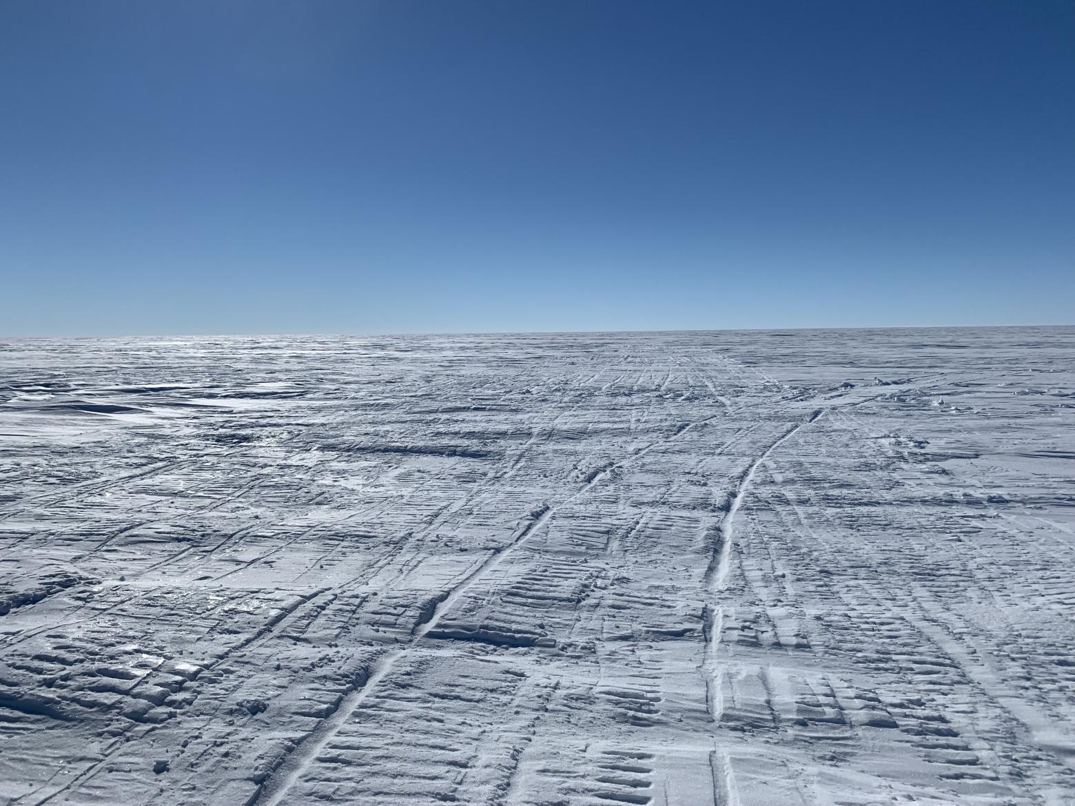 Frozen landscape of snow and ice with tire tracks from research vehicles in Antarctica.