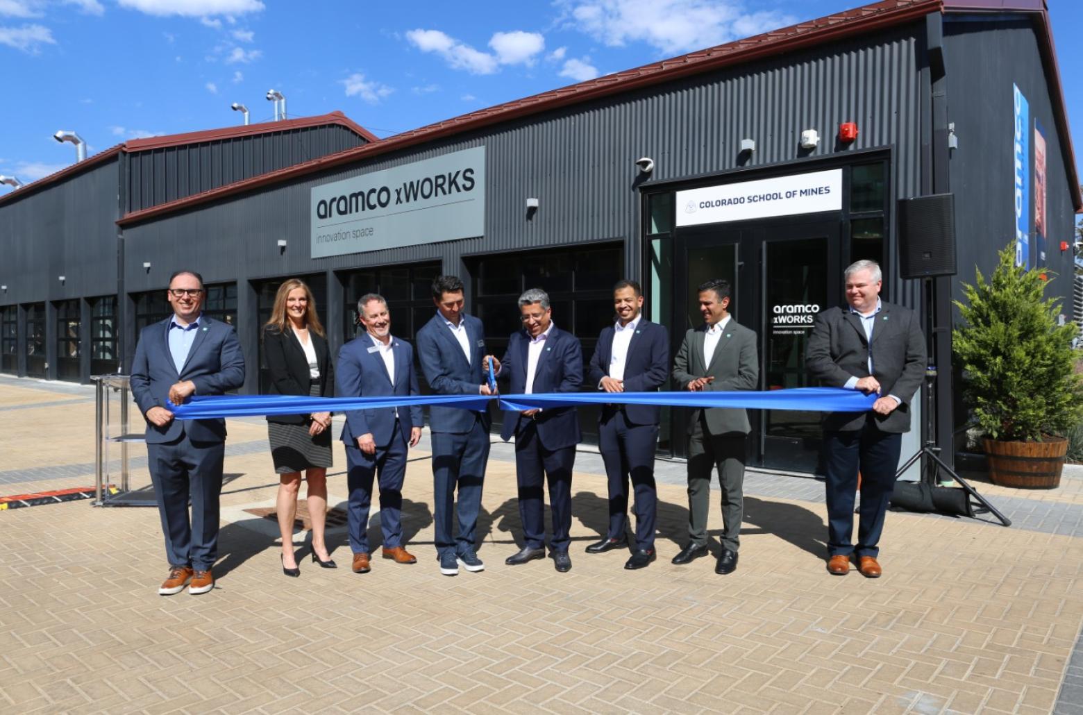 A row of people in suits cut a blue ribbon in front of a building