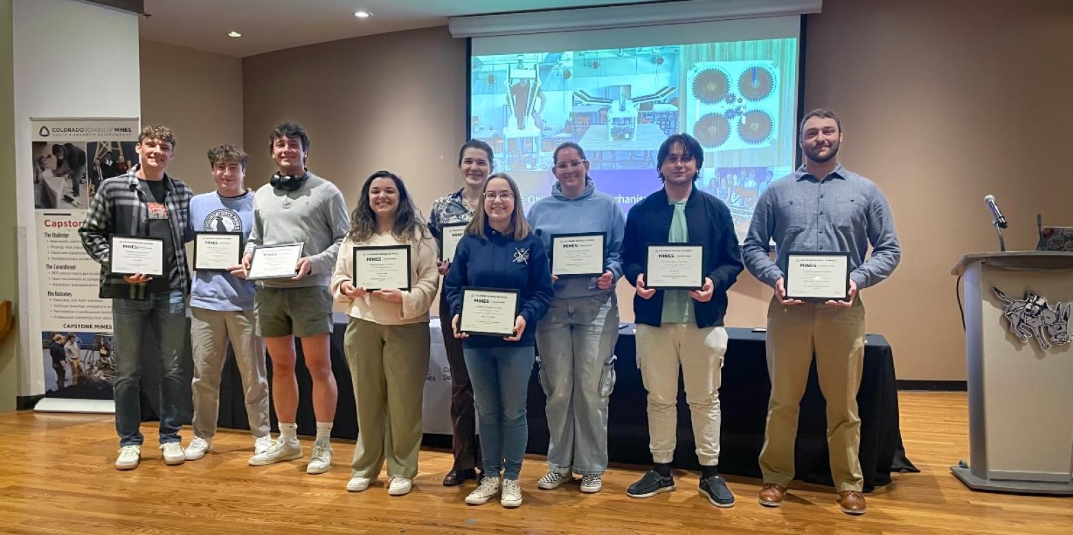 Group shot of students holding certificates in front of video screen
